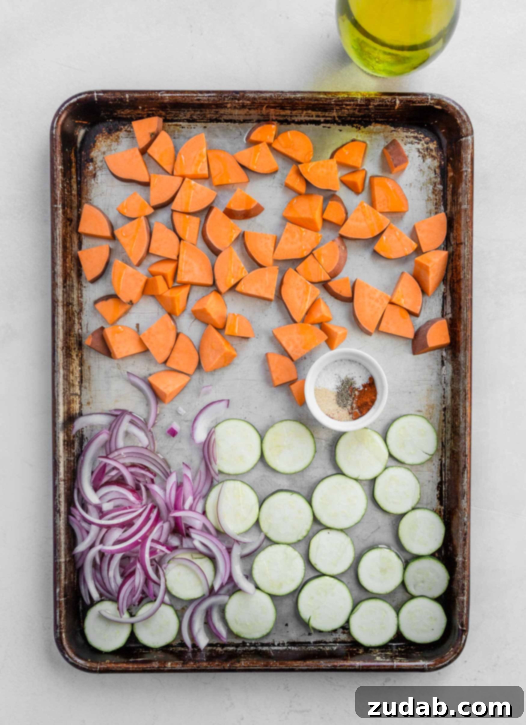 Plant Based Vegan Burrito Bowls A baking sheet with cubed sweet potato, red onions, and sliced zucchini.