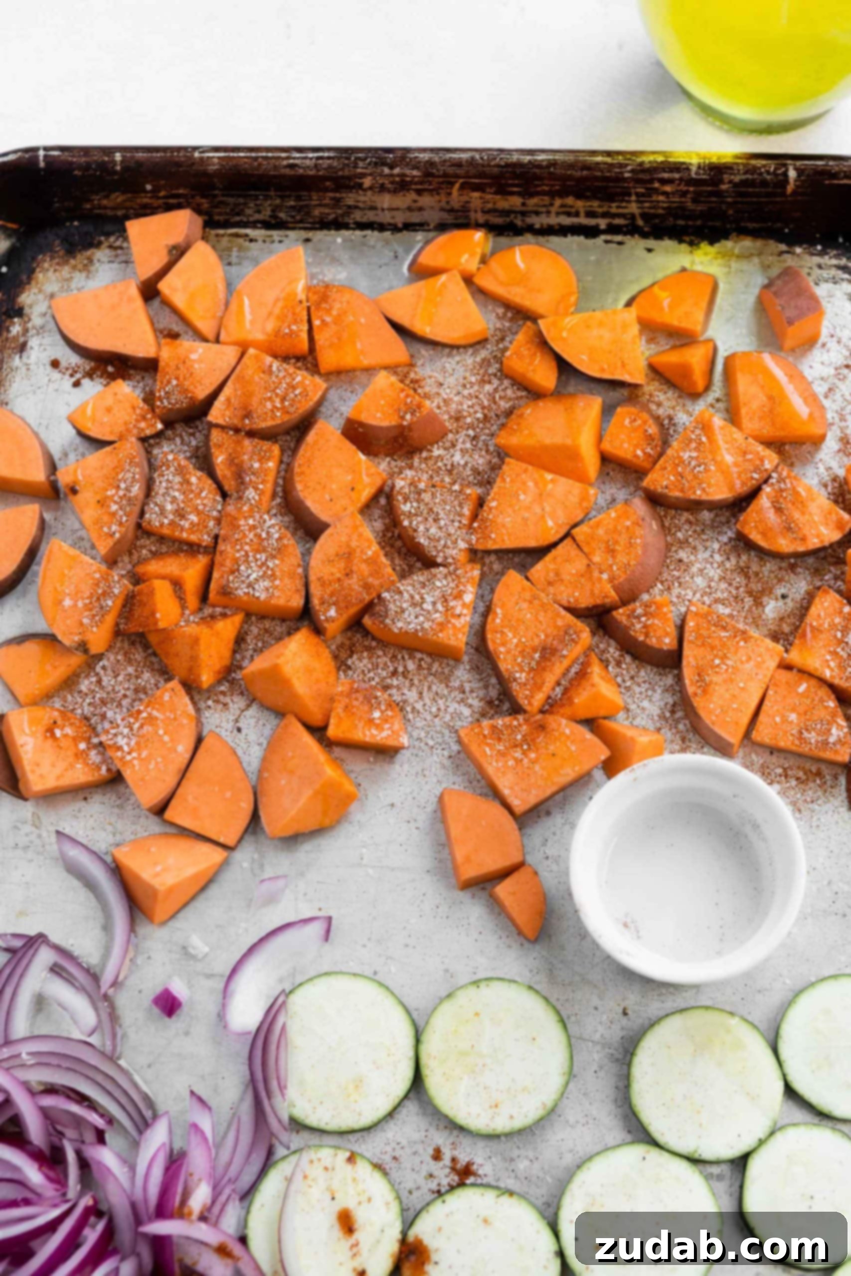 Plant Based Vegan Burrito Bowls Cubed sweet potatoes, red onions and zucchini on a baking sheet.