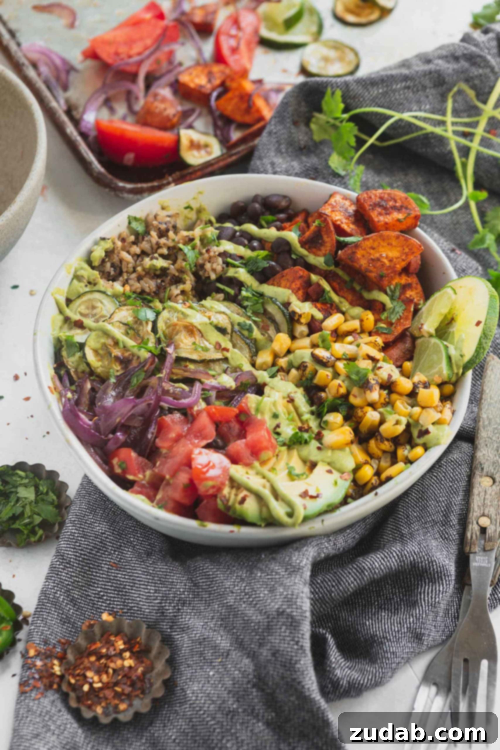 Flavor Fiesta Vegan Burrito Bowls 2 A vegan burrito bowl that contains tomatoes, avocados, roasted corn, sweet potatoes, zucchini and red onion. There is brown rice and quinoa in the burrito bowl.