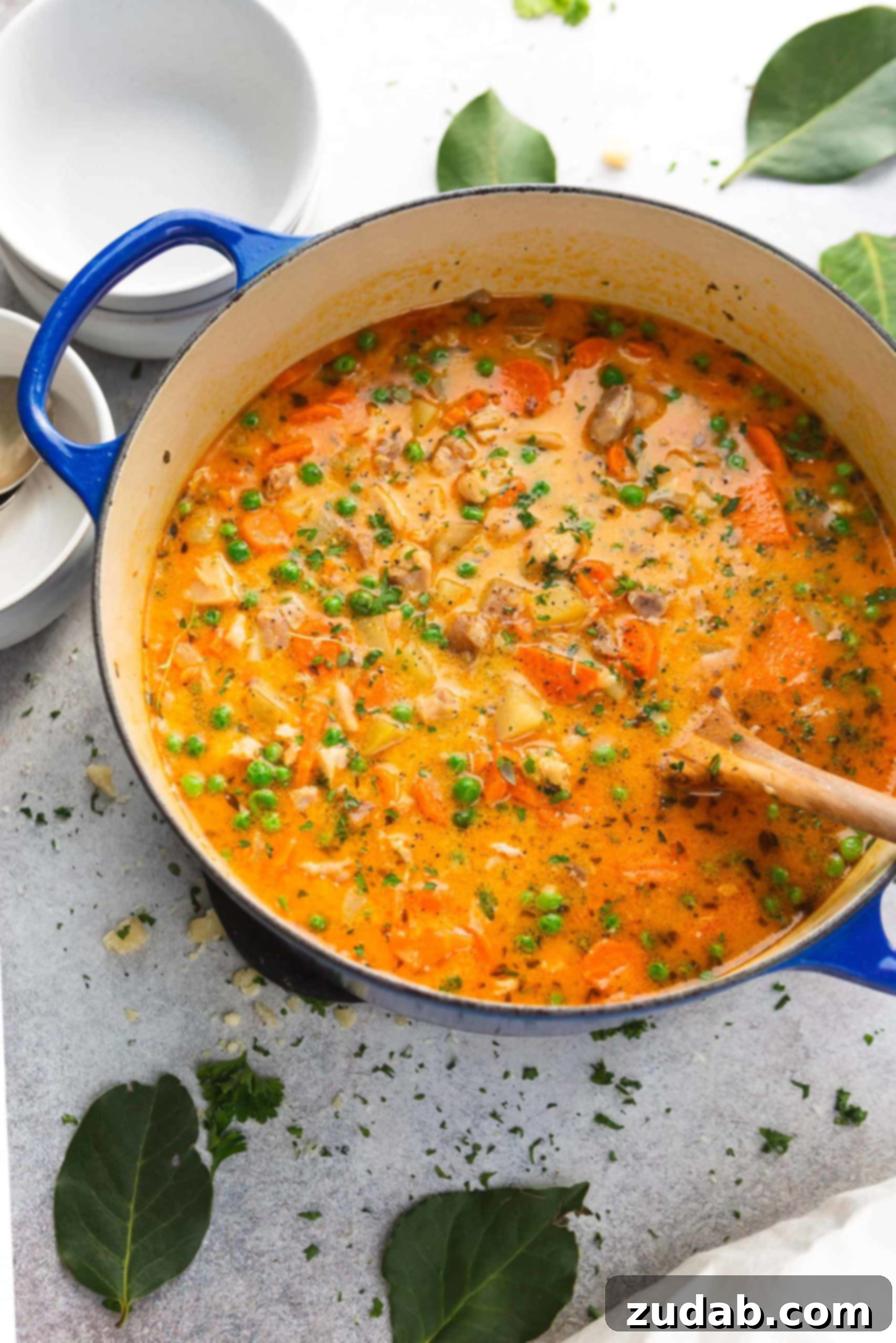 Slow Cooker Chicken Stew A pot of chicken stew. The stew is thick and bright colored with bits of celery, herbs, chicken and potatoes. A wooden spoon is in the pot and chopped herbs are on the counter top next to the pot.