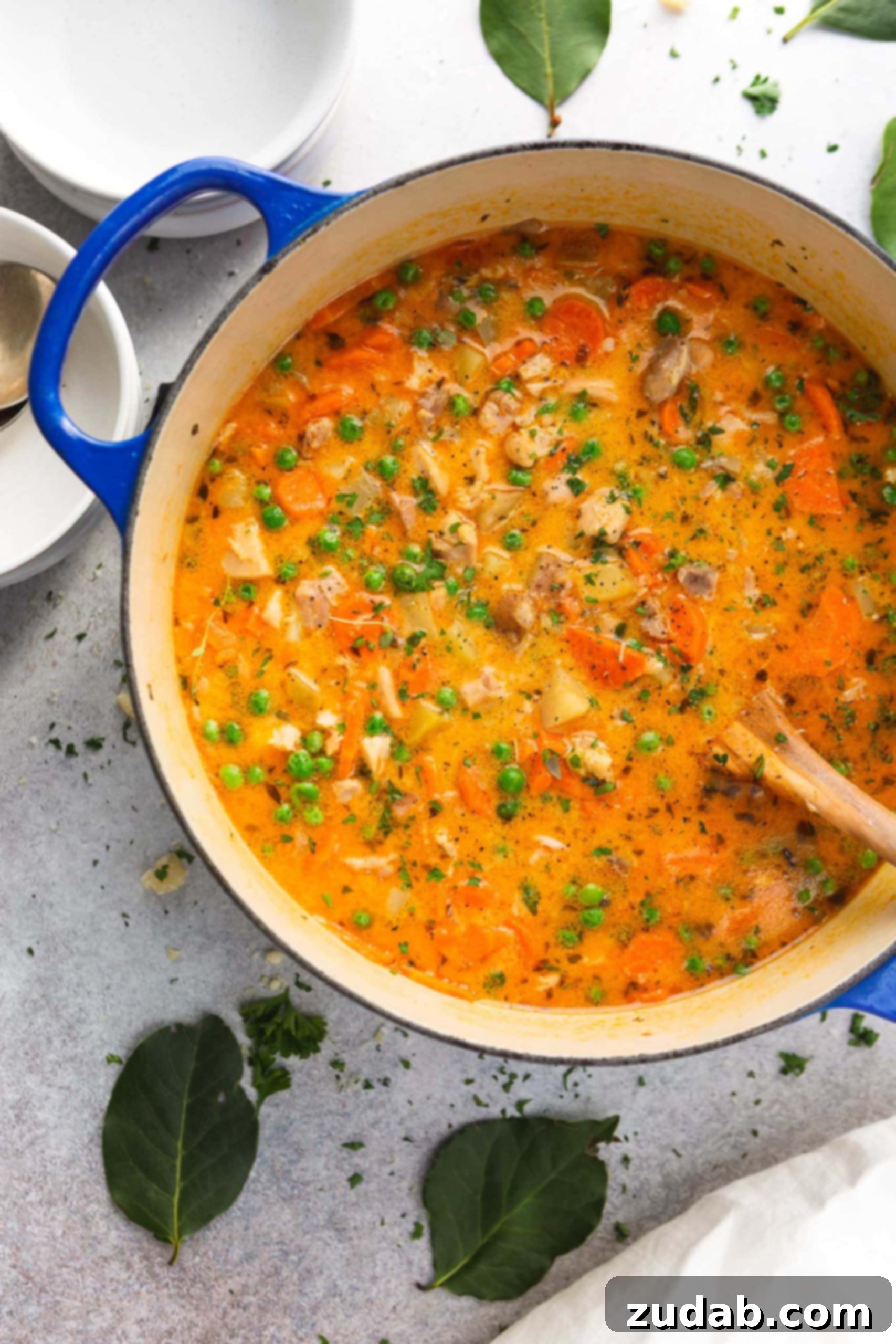 Hearty Slow Cooker Chicken Stew 4 A large pot of slow cooker chicken stew. It is a bright yellow-red color and packed with bits of fresh herbs, vegetables and chicken. A wooden spoon is in the pot.