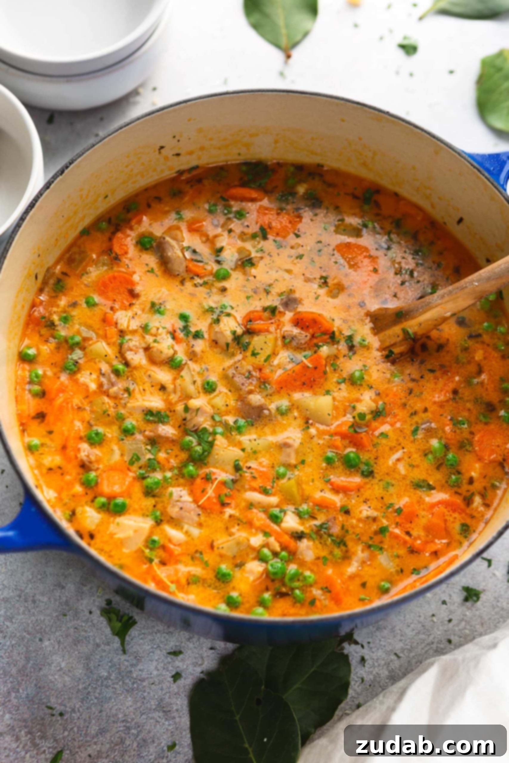 Hearty Slow Cooker Chicken Stew 5 A pot of thick slow cooker chicken stew with a wooden spoon in it. The stew is packed with bright vegetables, chicken and herbs.