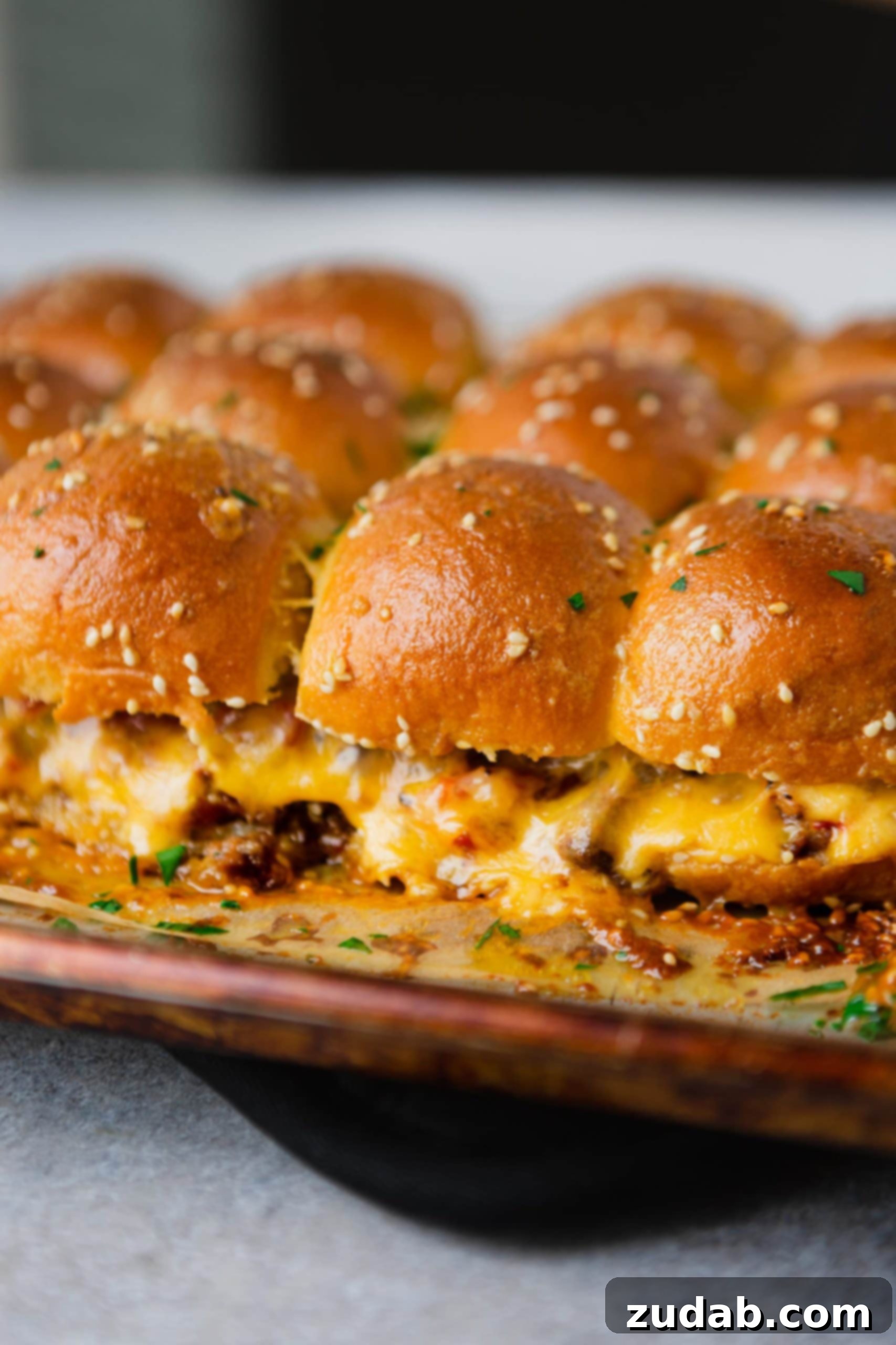 A pan of cheeseburger sliders. There is hamburger, and melted cheese on golden dinner rolls.