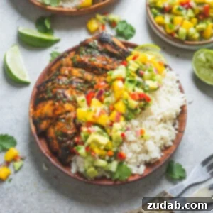 A top-down shot of a beautifully presented dinner featuring grilled cilantro lime chicken, a generous side of fluffy coconut rice, and a colorful mound of fresh mango salsa. The dish is garnished with fresh herbs and a lime wedge, highlighting its vibrant appeal.
