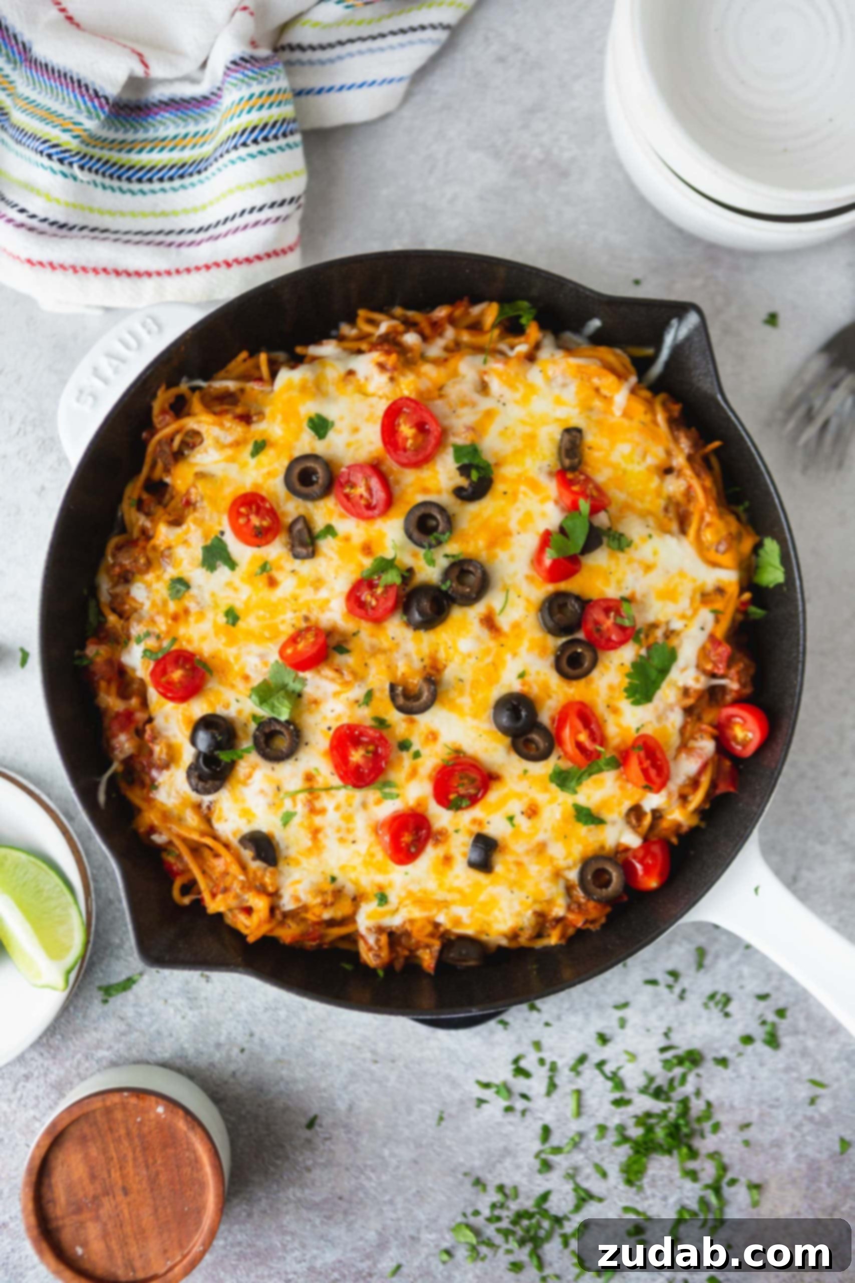 One Pot Cheesy Ground Beef Taco Spaghetti A cast iron skillet filled with cheesy ground beef taco spaghetti. It is topped with cheese, olives, green onion, tomatoes and cilantro.