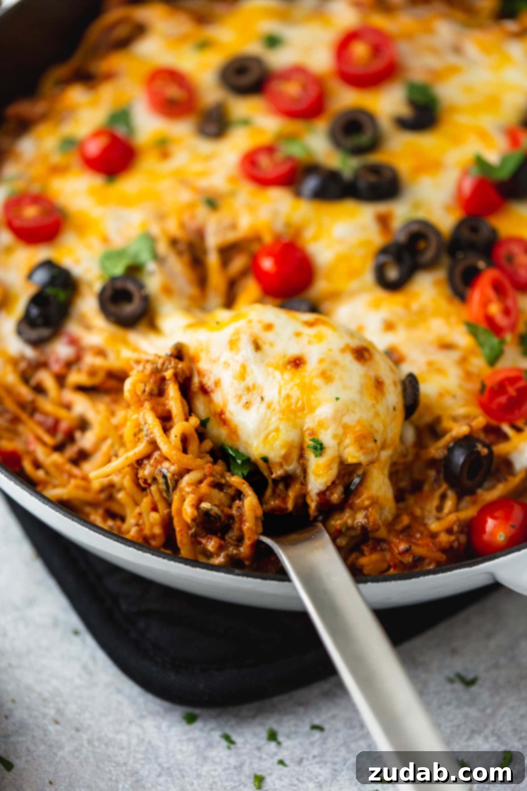 One Pot Cheesy Ground Beef Taco Spaghetti A skillet full of cheesy ground beef taco spaghetti. A serving spoon is in the pot and the spaghetti is topped with melted cheese, tomatoes, olives, green onions and cilantro.
