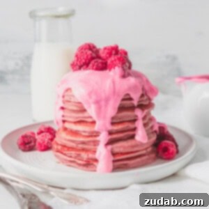 A stack of healthy pink pitaya blender pancakes, covered with pink sauce.