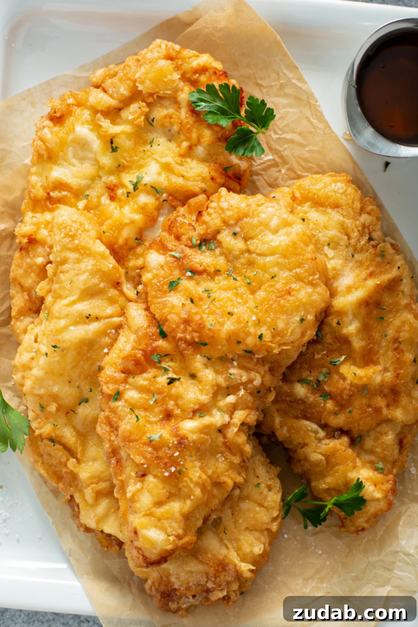 A serving platter heaped with golden fried chicken. A few parsley leaves are scattered on top.