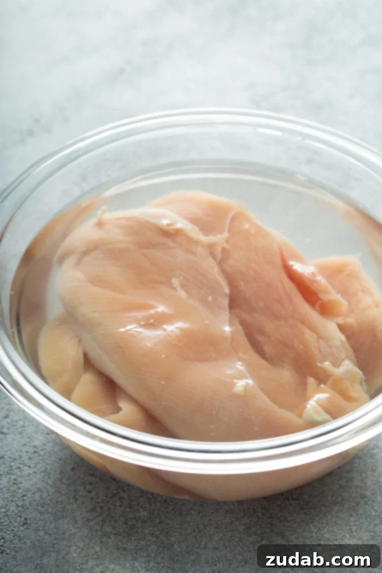 Uncooked chicken breasts in a bowl of salt water.
