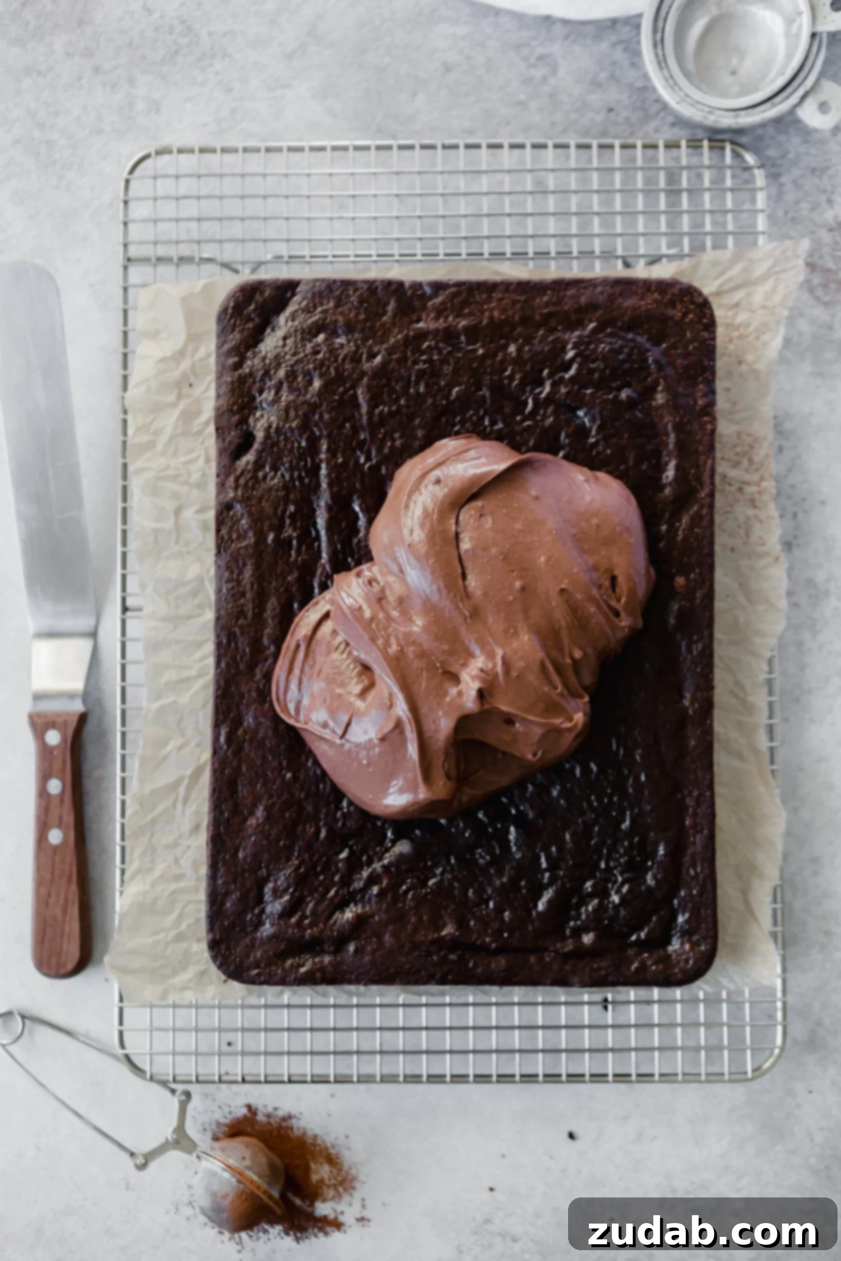 Homemade Chocolate Mayonnaise Cake A 9x13 chocolate mayonnaise cake. There is a mound of chocolate frosting in the middle that has not been spread over the cake yet. A frosting spatula is next to the cake.