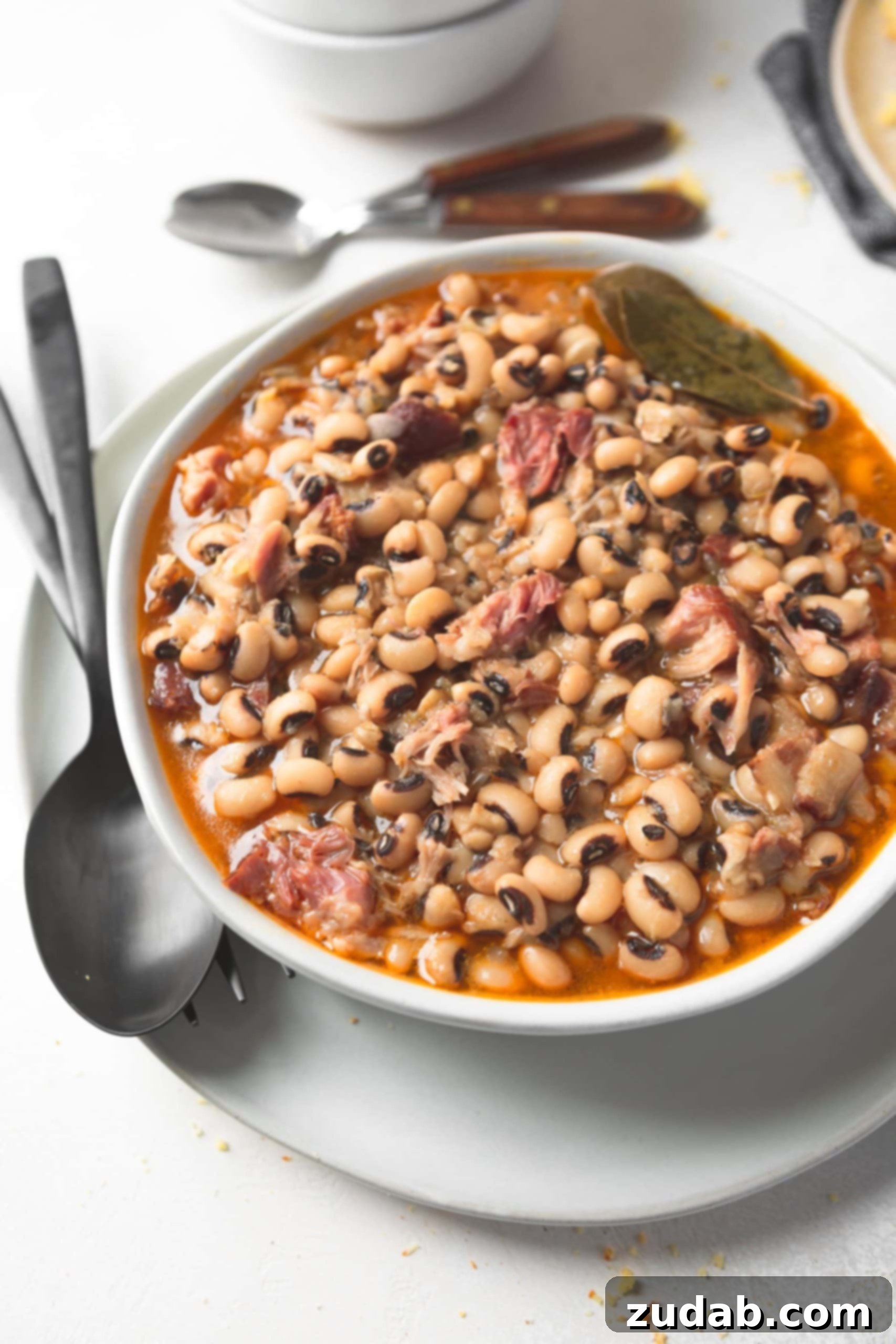 A bowl of southern black eyed peas. A spoon and fork are sitting next to the bowl.