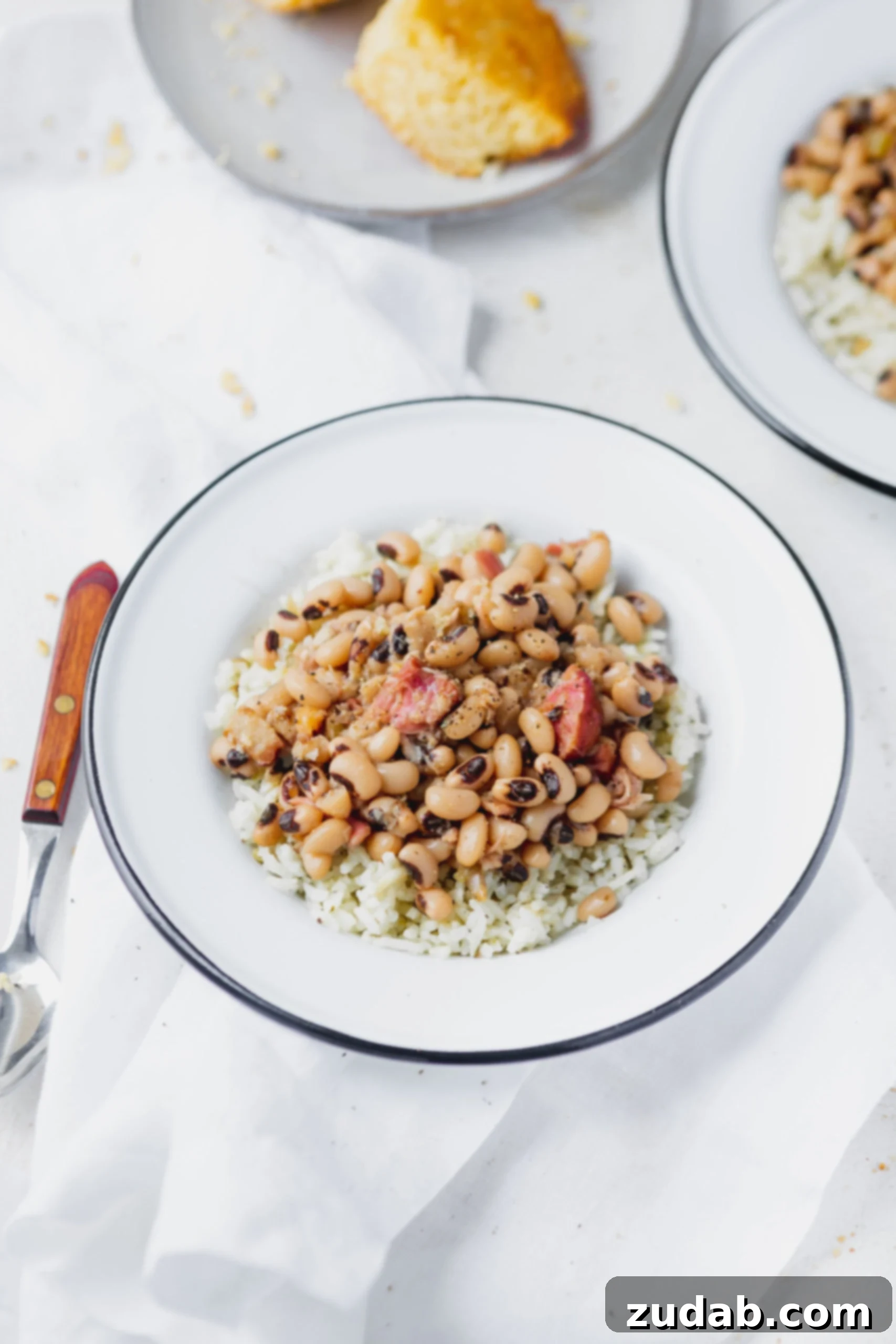 Instant Pot Black Eyed Peas A plate of instant pot black eyed peas over rice. There is a spoon next to the plate and a plate of cornbread in the background.