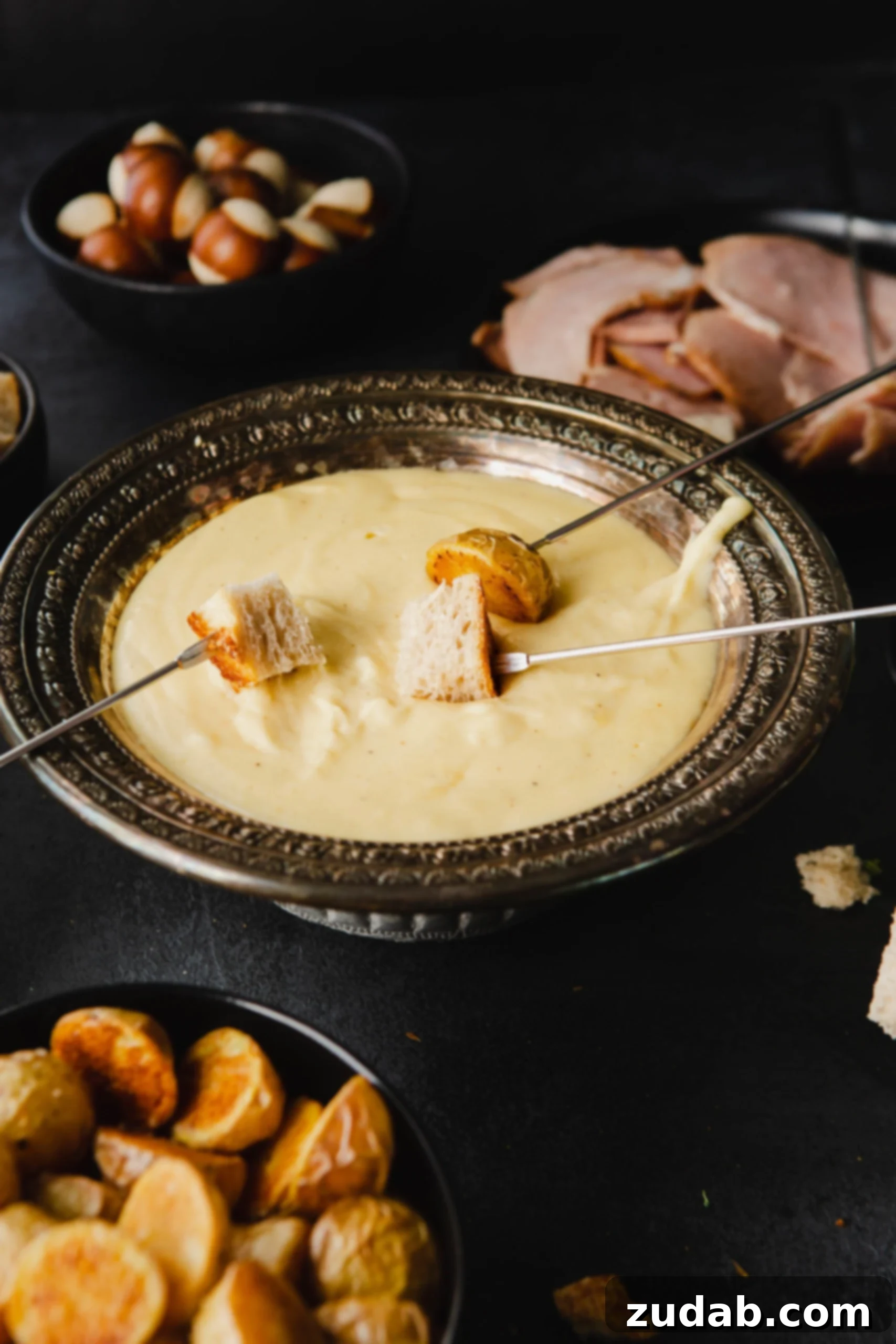 Perfect Cheese Fondue and What to Dip in Fondue A bowl of cheese fondue with skewers of bread being dipped in the cheese. Fruit, bread meat and vegetables to dip are around the bowl.
