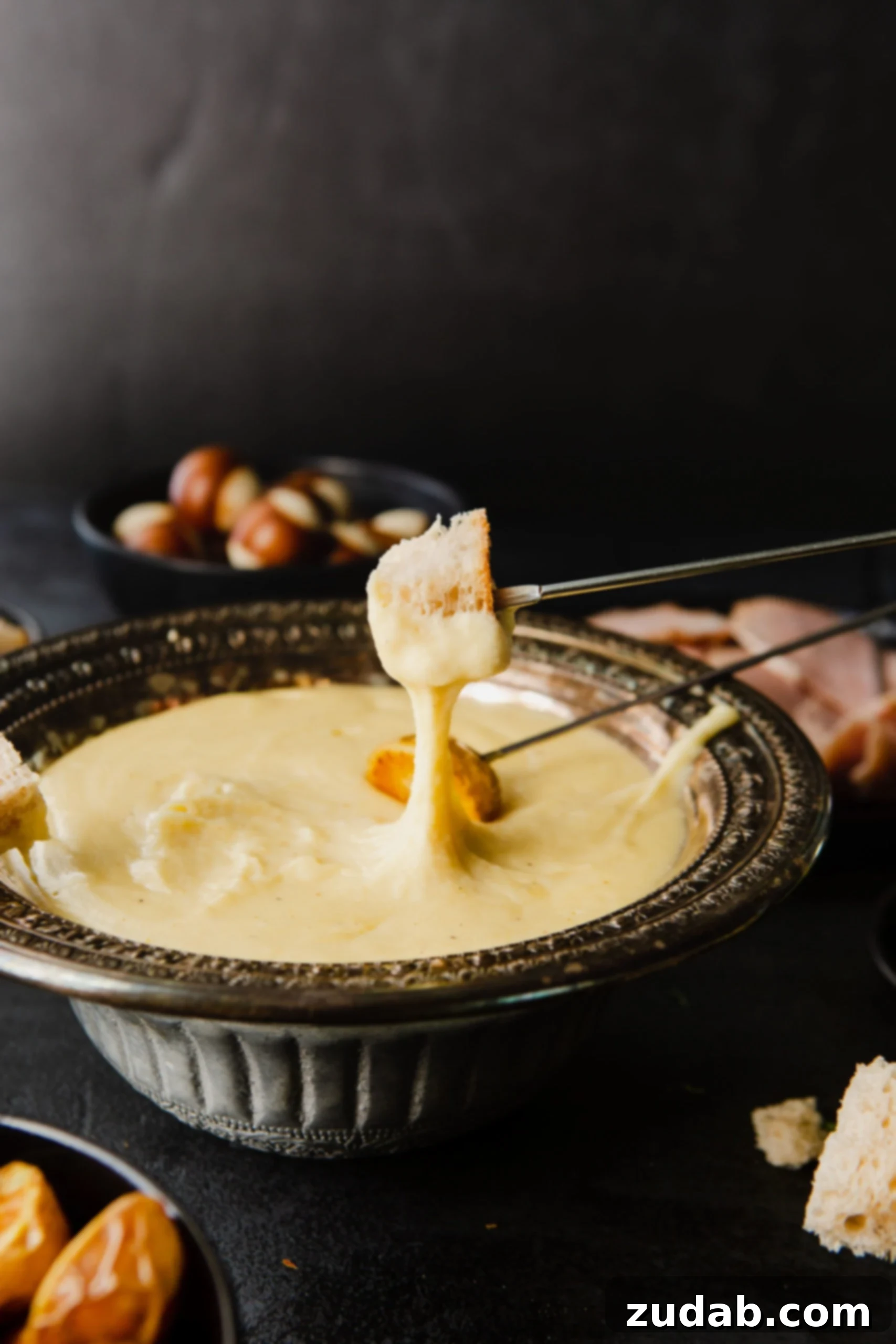 Perfect Cheese Fondue and What to Dip in Fondue A skewer of bread that has been dipped in cheese fondue. the skewer is being held above the bowl of fondue.