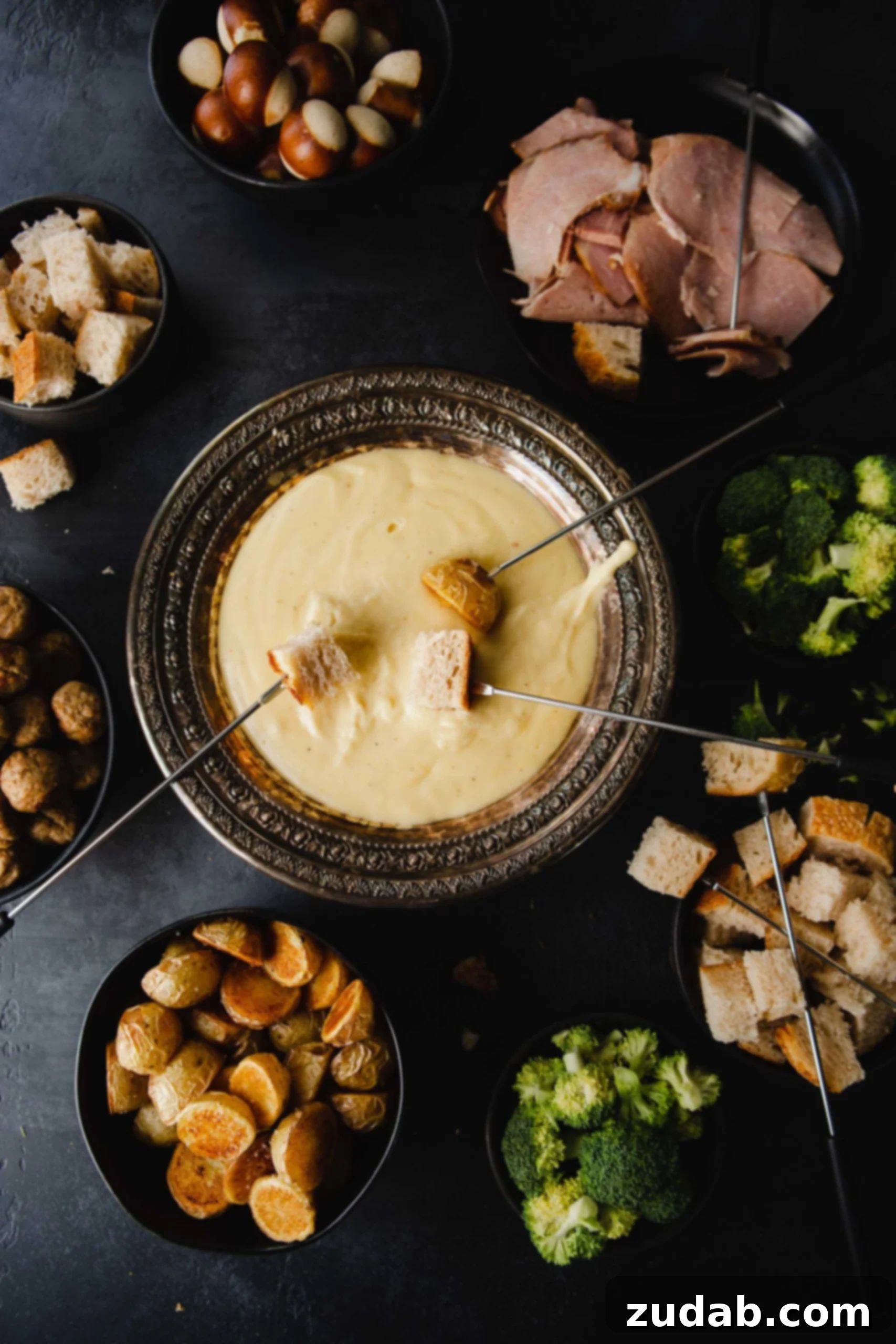 Perfect Cheese Fondue and What to Dip in Fondue A bowl of cheese fondue with skewers of bread being dipped in. The fondue is surrounded by other things that are perfect for dipping, such as meat, fruit, bread and vegetables.