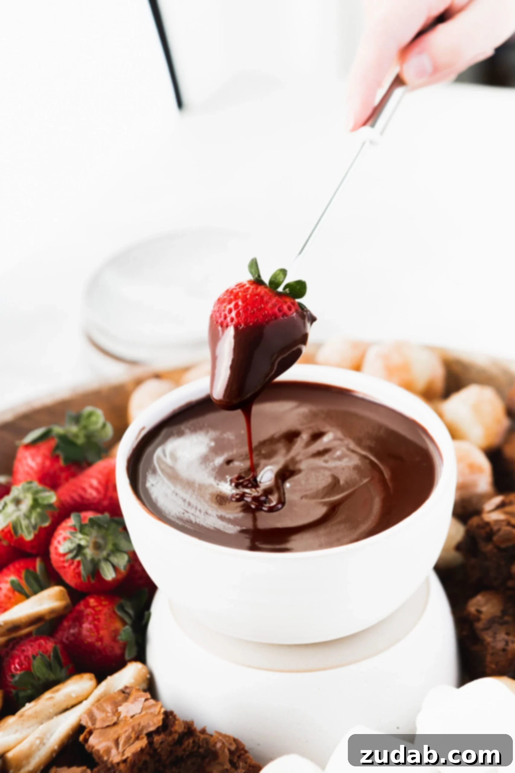 Chocolate Fondue A bowl of rich chocolate fondue with a fresh strawberry just dipped into its luscious depths. Other fresh strawberries and sweet donut holes are visible in the soft-focus background, inviting more dipping.