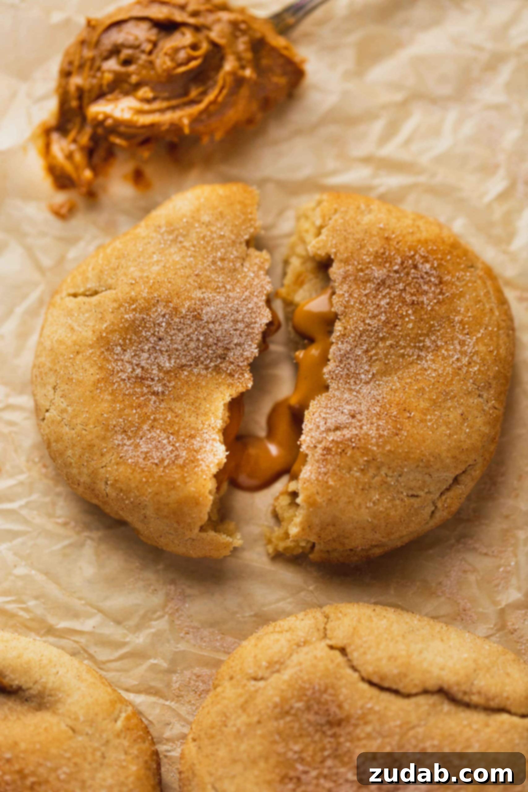 Biscoff Stuffed Snickerdoodle Cookies A biscoff stuffed snickerdoodle that is broken in half showing the biscoff oozing our from inside.