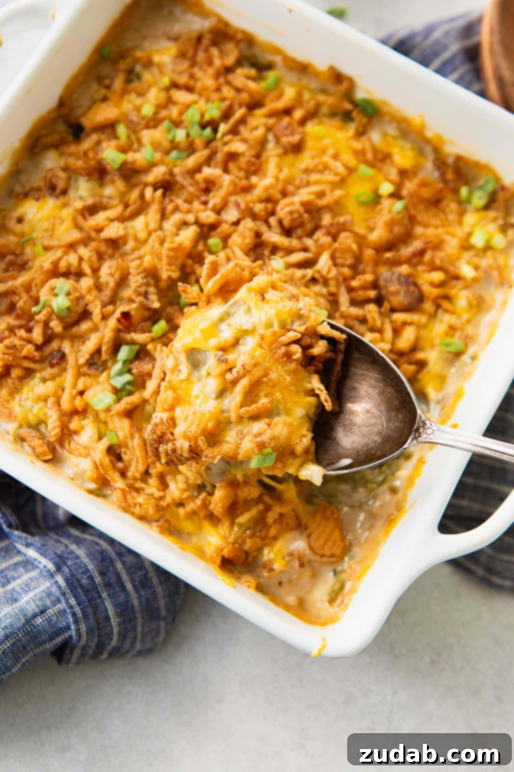 Ultimate Classic Green Bean Casserole 5 A freshly baked classic green bean casserole in a white baking dish, ready to be served. The top is covered with a golden-brown layer of crispy French fried onions, and the creamy green beans are visible underneath, promising a comforting and flavorful side dish.