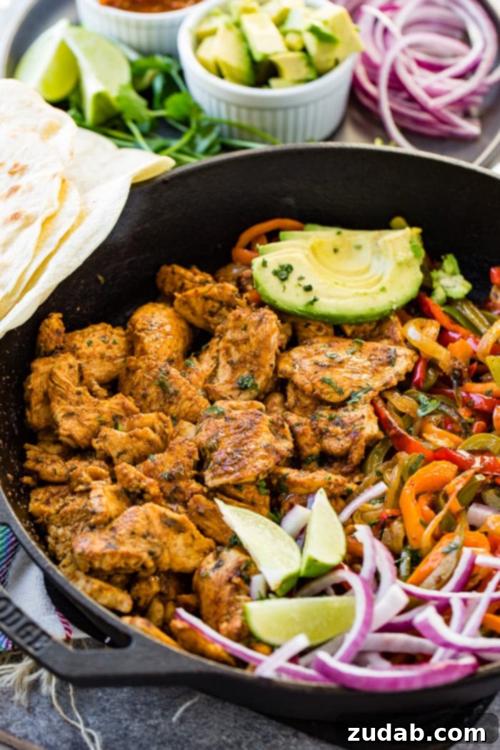Over 25 Healthy Recipes 15 A cast iron skillet brimming with sizzling chicken fajita filling, featuring seasoned chicken, sautéed peppers and onions, lime wedges, and sliced avocado.