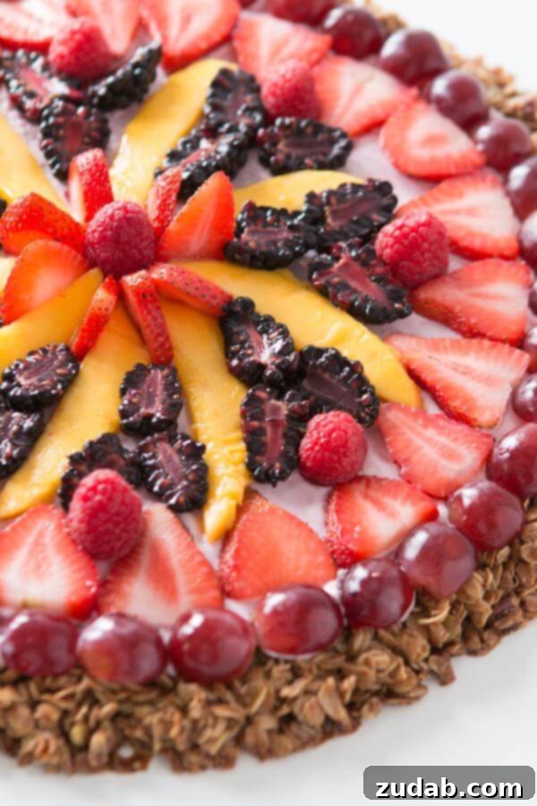Over 25 Healthy Recipes 5 A vibrant breakfast fruit and yogurt pizza topped with fresh berries, granola, and creamy yogurt sauce, set on a dark surface.
