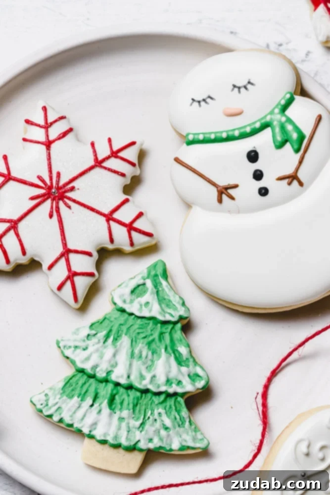 The Best Royal Icing for Holiday Cookies 2 Christmas sugar cookies adorned with delicate royal icing. Featuring a charming snowman with a green scarf, a festive tree with green icing and white snow accents, and an elegant white star with intricate red designs.