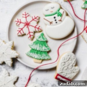 The Best Royal Icing for Holiday Cookies 11 A plate with Christmas sugar cookies decorated with royal icing. There is a snowman with a green scarf, a white mitten with red trim, a green tree with white snow accents, and a white star with red accents. A red ribbon is draped over the edge of the plate.