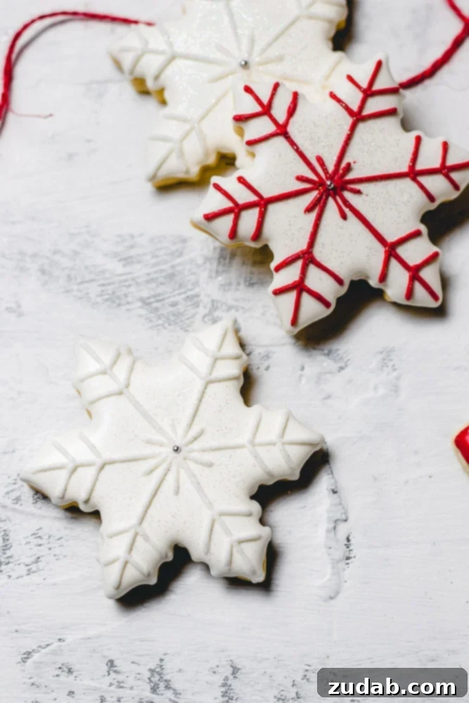 The Best Royal Icing for Holiday Cookies 3 Beautifully decorated Christmas sugar cookies featuring two intricate snowflakes, one with elegant white accents and another with striking red details.