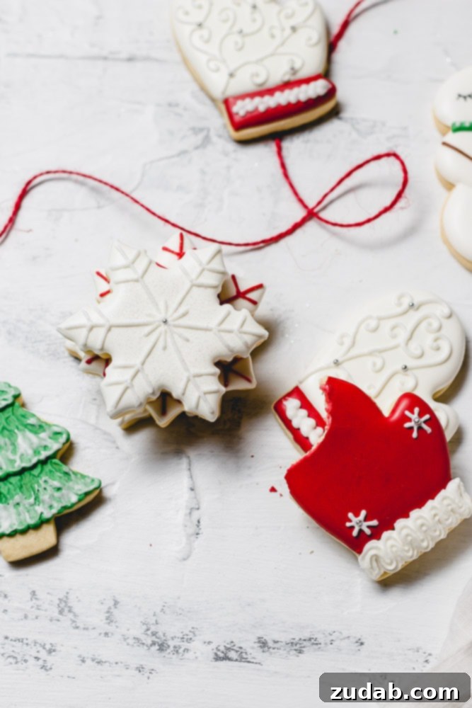 The Best Royal Icing for Holiday Cookies 8 An array of beautifully decorated Christmas sugar cookies with royal icing. The collection includes delicate white snowflakes, festive red mittens, elegant white mittens with red trim, and a classic green tree adorned with white snow.
