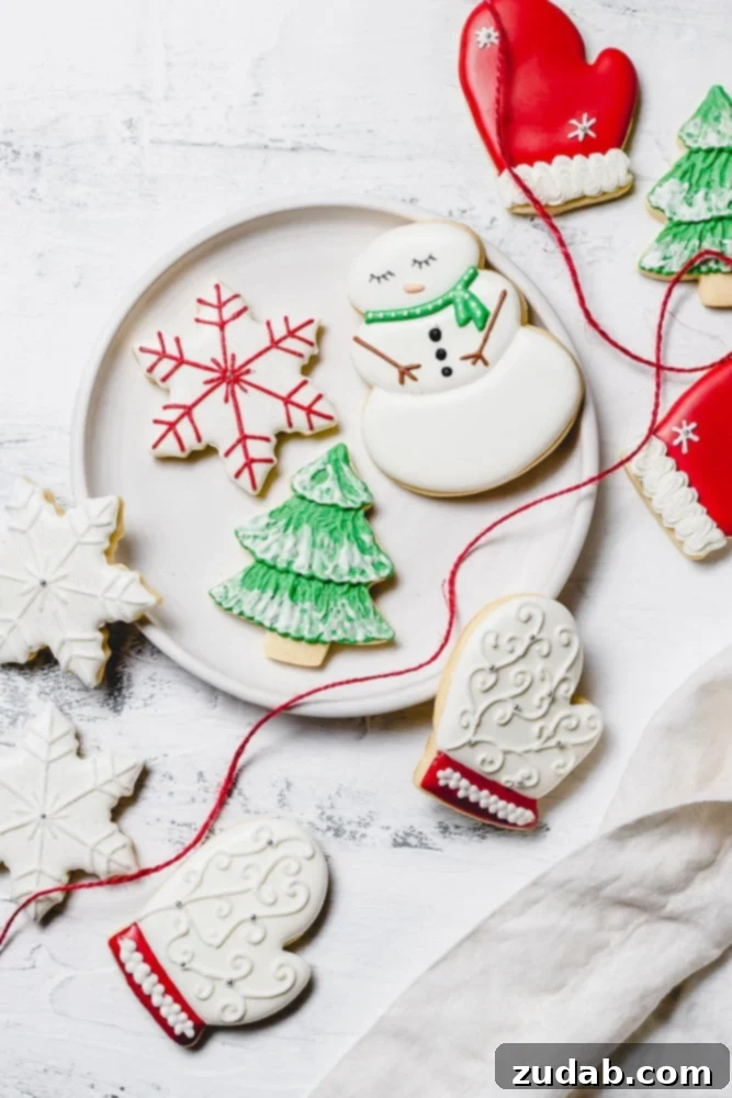 The Best Royal Icing for Holiday Cookies 10 A festive plate showcasing an assortment of Christmas sugar cookies adorned with royal icing. Designs include a cheerful snowman with a green scarf, a delicate snowflake with red accents, a classic green tree dusted with white snow, a cozy white mitten with red trim, and multiple pristine white snowflakes.
