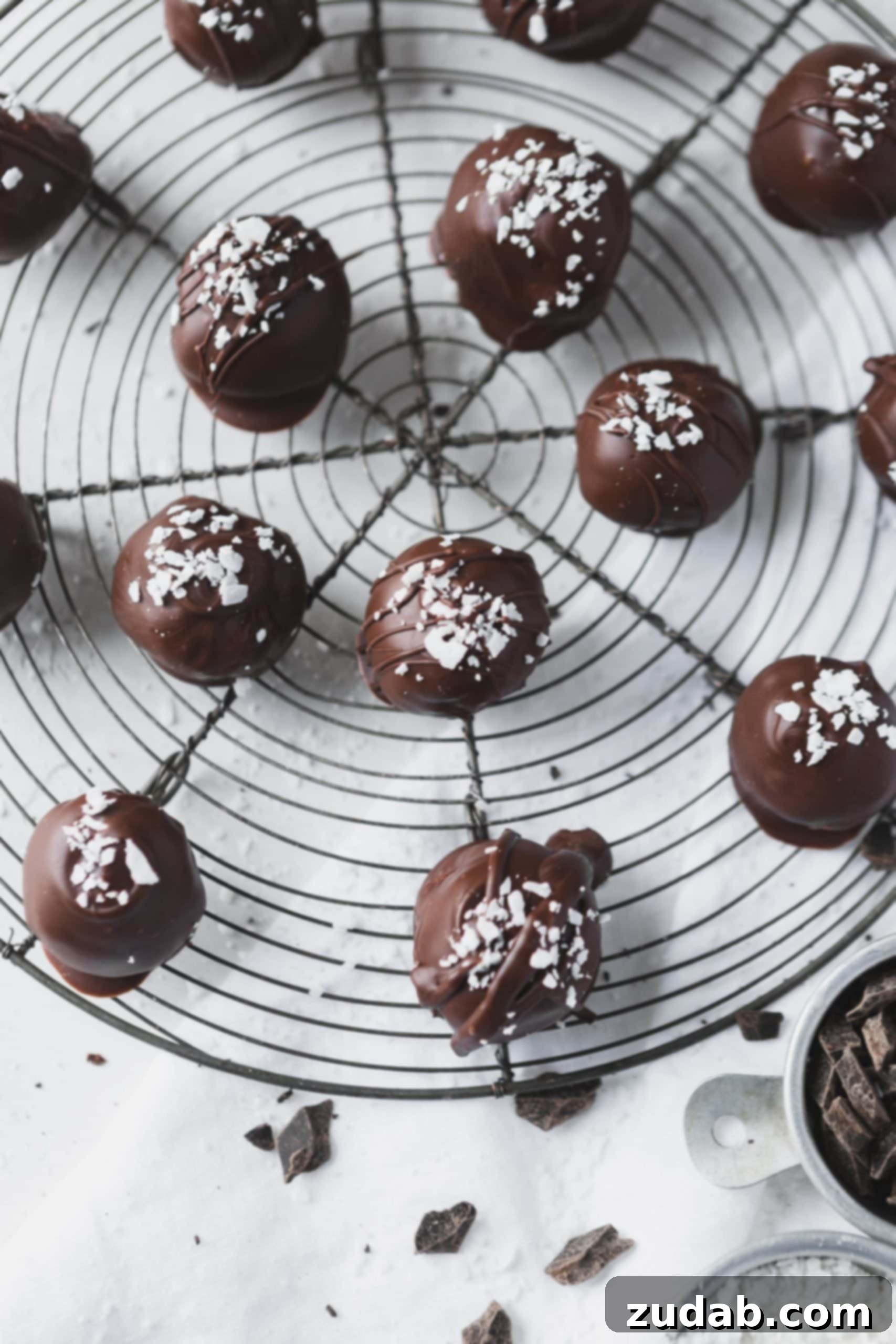 Chocolate Covered Coconut Balls A round wire rack with chocolate covered coconut balls. There are a few coconut flakes sprinkled on top.
