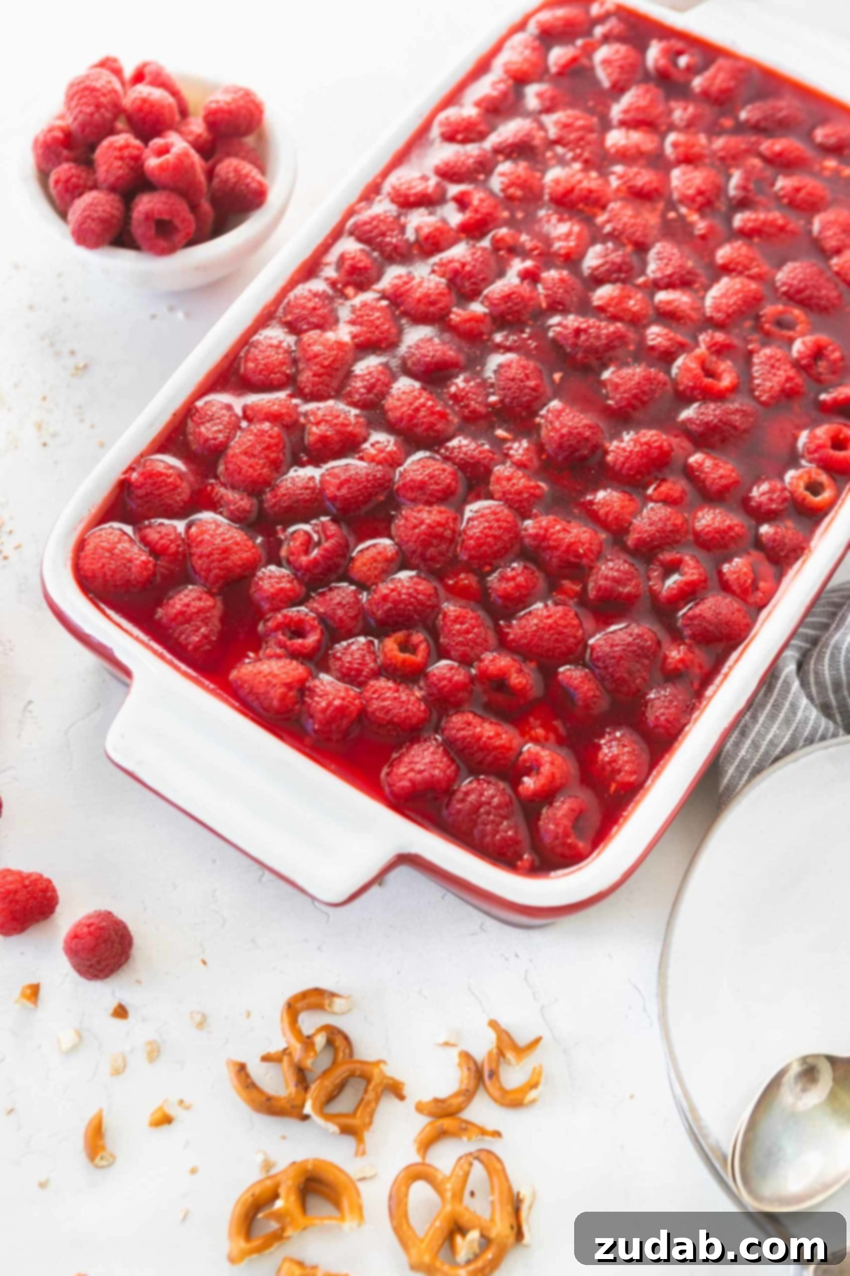 Raspberry Pretzel Jello Salad A raspberry pretzel jello salad in a white casserole dish. You can see the red jello layer filled with fresh raspberries.
