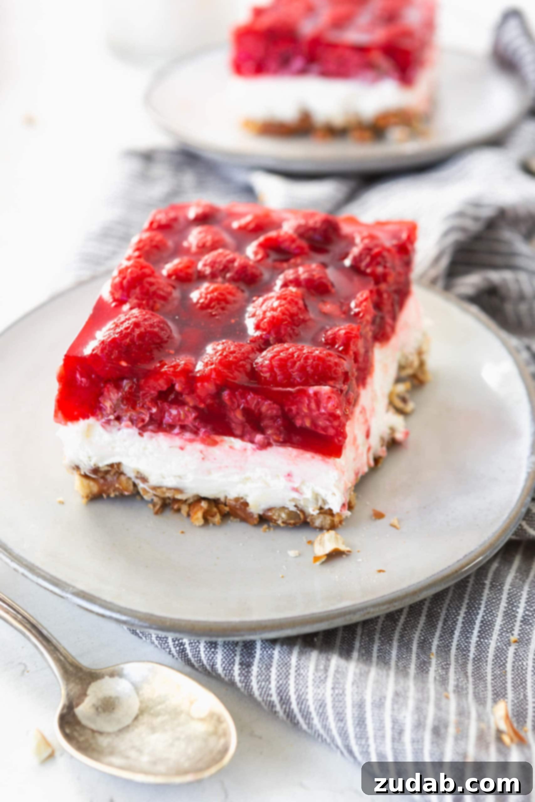 Raspberry Pretzel Jello Salad A serving of raspberry pretzel salad on a white salad plate. You can see the three layers in the salad. Pretzel layer on bottom, creamy filling next, and raspberry jello with fresh raspberries on top.