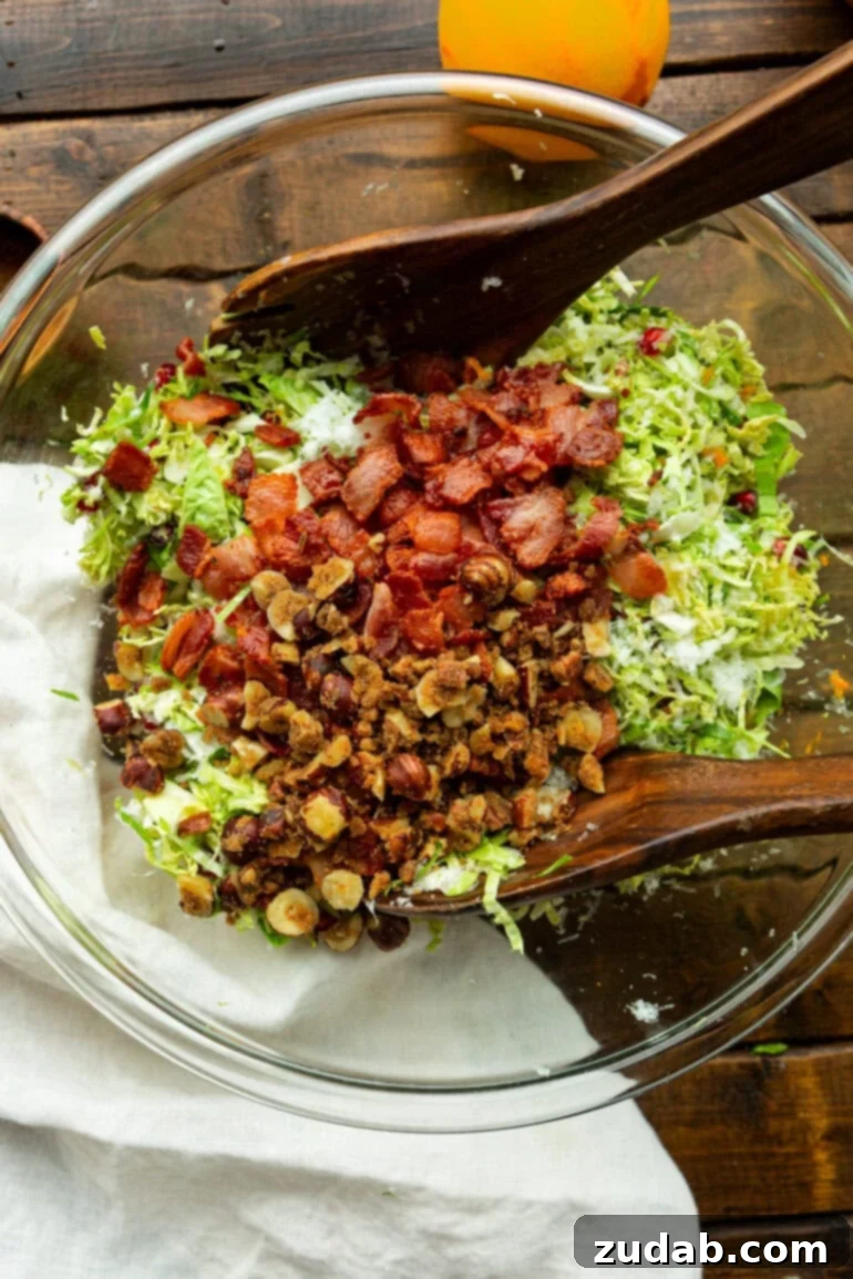 Jeweled Pomegranate Brussels Sprout Salad 3 A clear glass bowl filled with a vibrant pomegranate Brussels sprout salad, highlighting the glistening candied nuts and ruby-red pomegranate arils mixed within the finely shredded Brussels sprouts and crispy bacon.