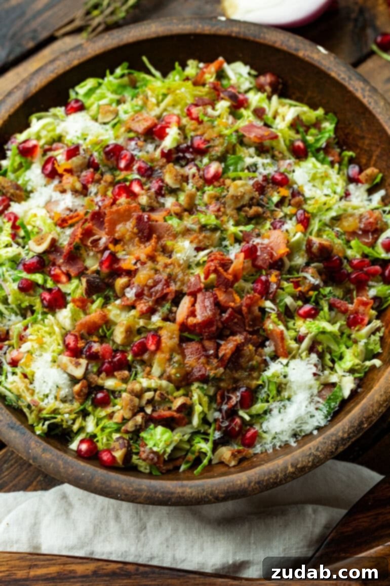 Jeweled Pomegranate Brussels Sprout Salad 7 An untossed pomegranate and Brussels sprout salad, revealing layers of fresh Brussels sprouts, crispy bacon bits, sweet candied nuts, and vibrant pomegranate arils, ready to be dressed.