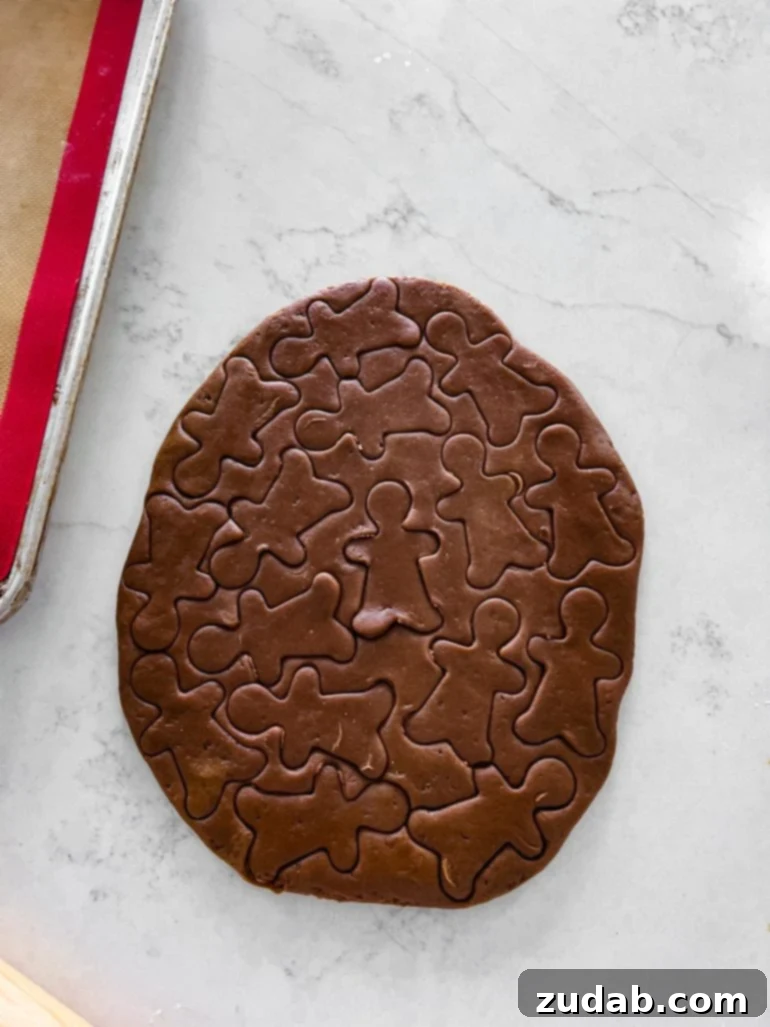Ultimate Soft and Chewy Christmas Gingerbread Man Cookies 4 A festive image of gingerbread cookie dough rolled out on a clean countertop, dotted with numerous freshly cut little gingerbread men shapes. I love making little gingerbread boys so that I can eat a dozen of them and feel less bad about it! Ha! #gingerbreadmen #gingerbreadcookies #christmascookies