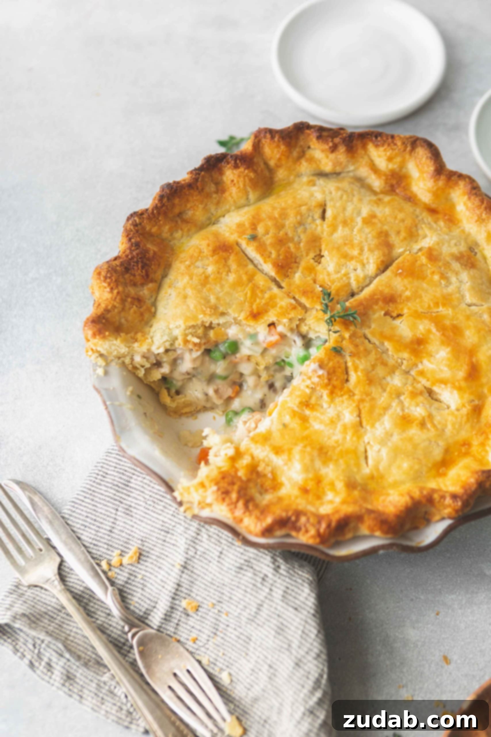 Turkey Pot Pie A baked turkey pot pie with a slice removed. The crust is a golden brown and you can see the creamy filling with peas, carrots and turkey. Two forks are next to the pie.