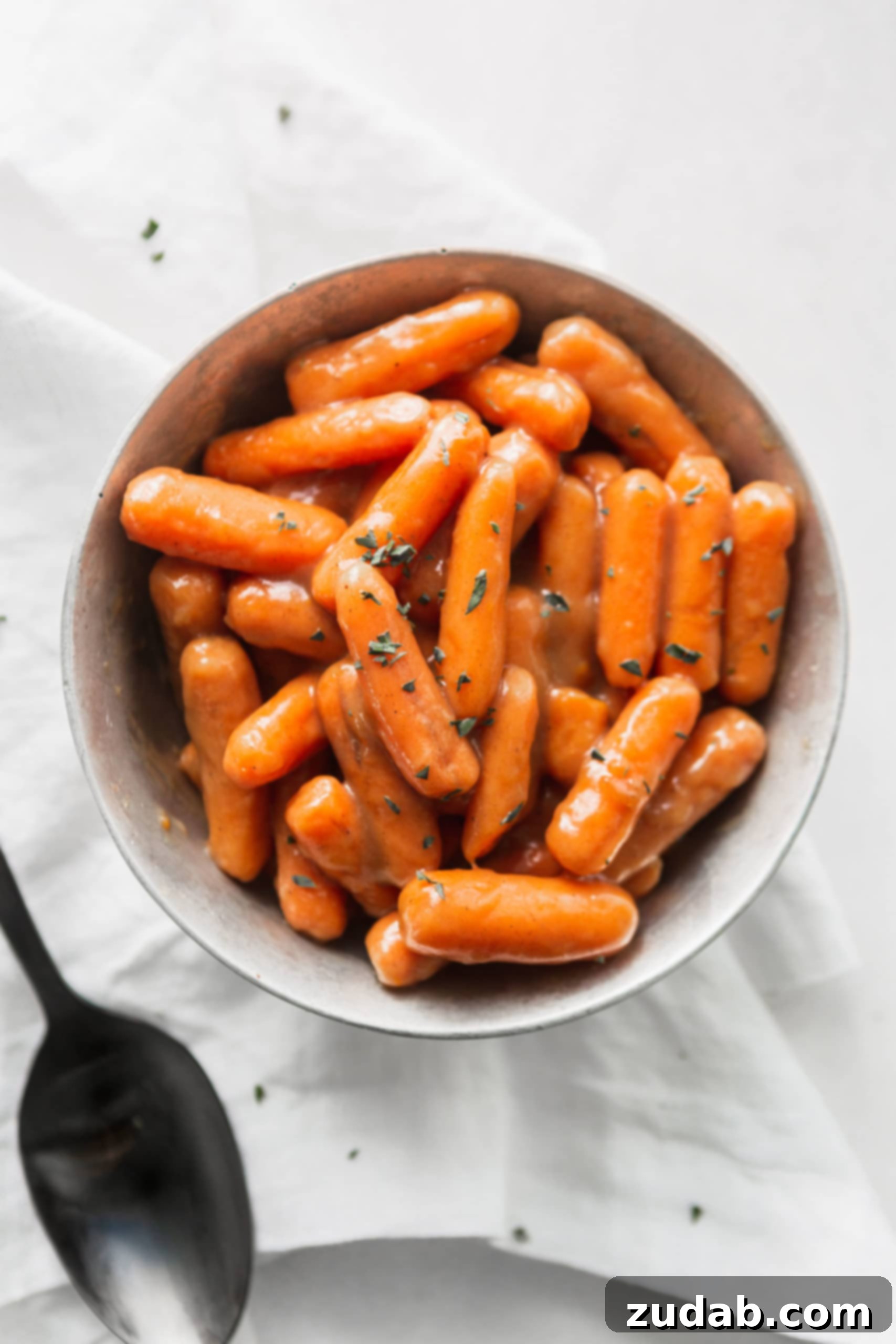 Slow Cooker Orange Glazed Carrots A bowl of orange glazed baby carrots. A serving spoon is next to the bowl.