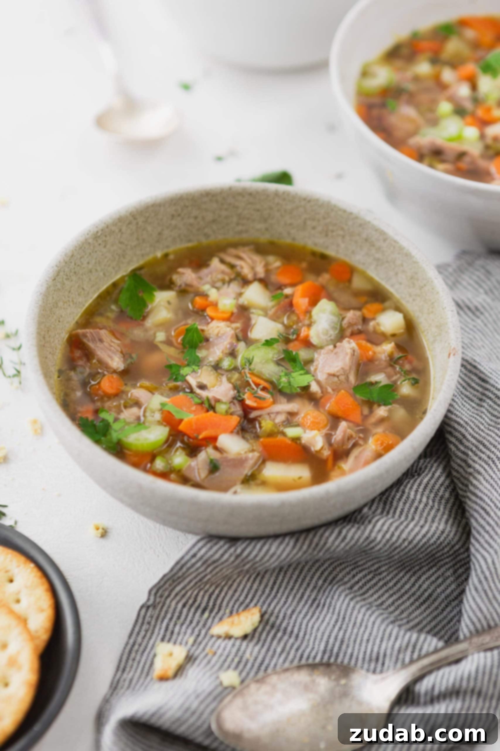A bowl of left over turkey soup. The soup has chunks of turkey, slices of carrots and celery and herbs in a turkey broth.