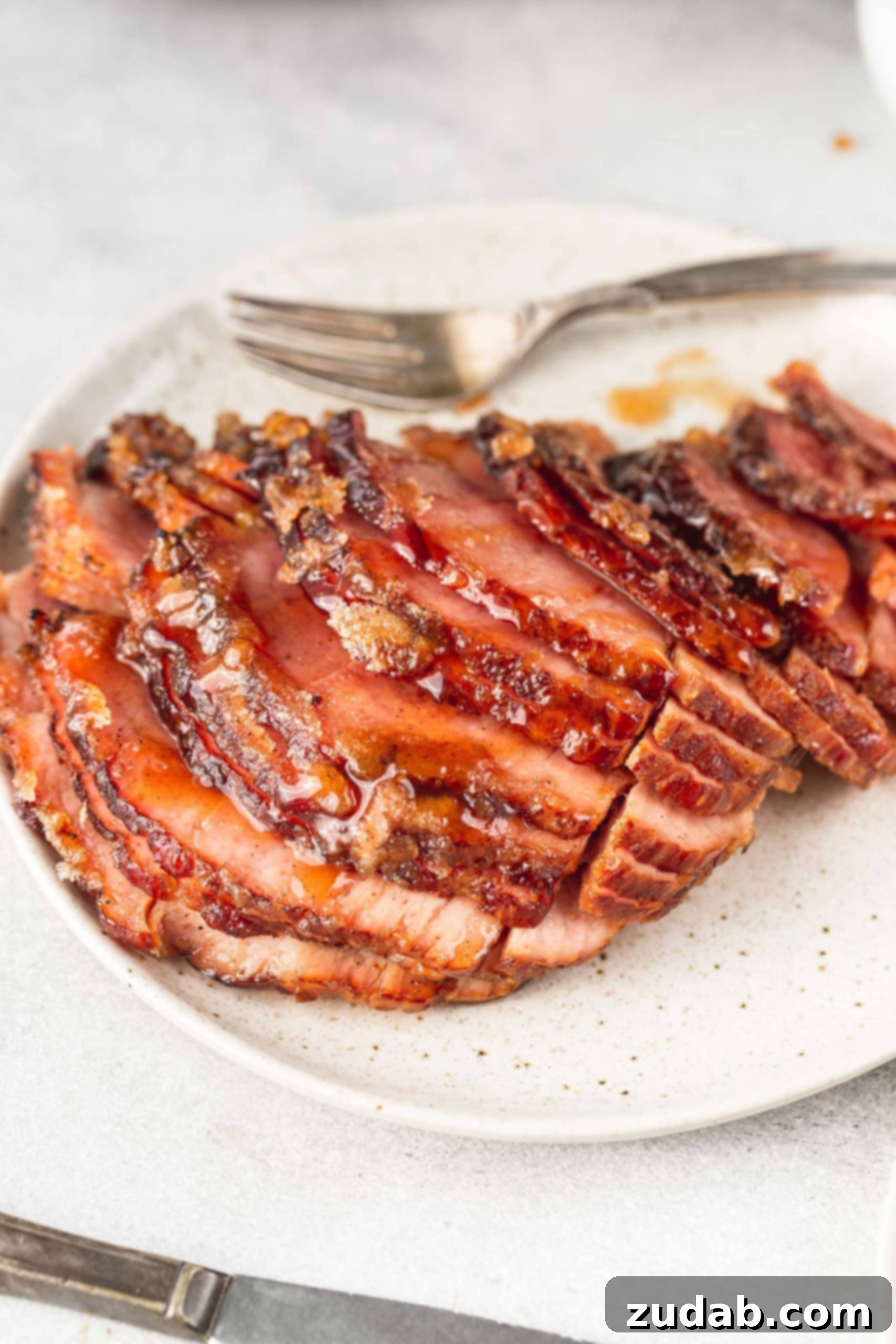 A spiral-cut honey glazed ham resting on a festive serving platter, with a fork nearby. The rich glaze and tender slices promise a delicious experience.
