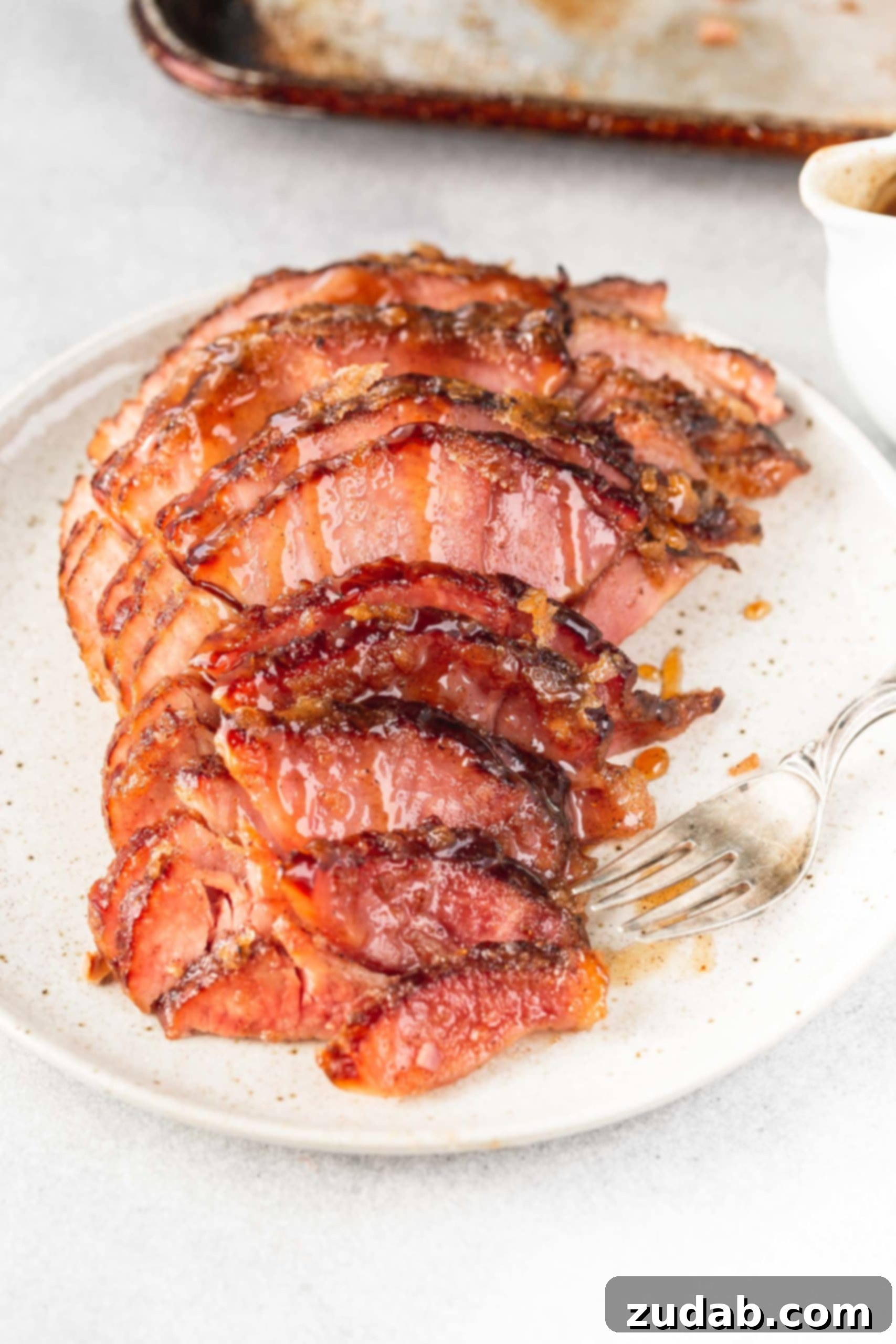 A perfectly carved spiral-cut honey glazed ham on a serving plate, with slices gently separated to show the juicy interior and shiny glaze.