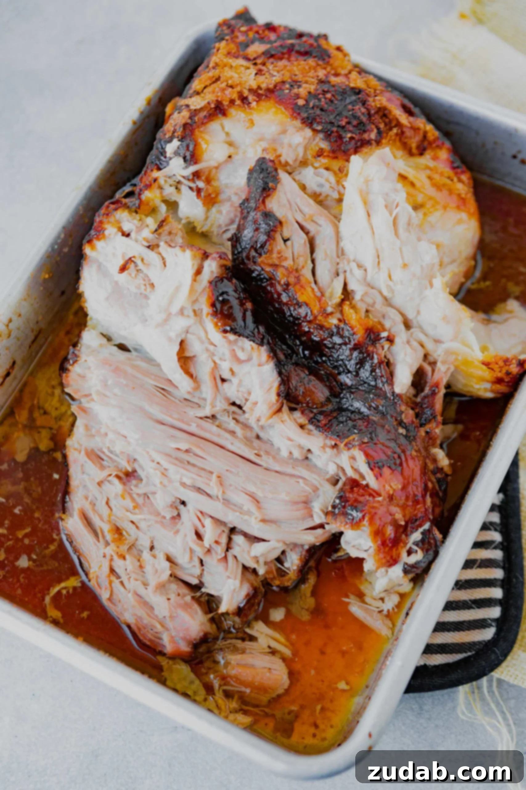 Slow Cooker Kalua Pork Recipe a photo of a tender pork roast starting to be shredded in a white baking dish.