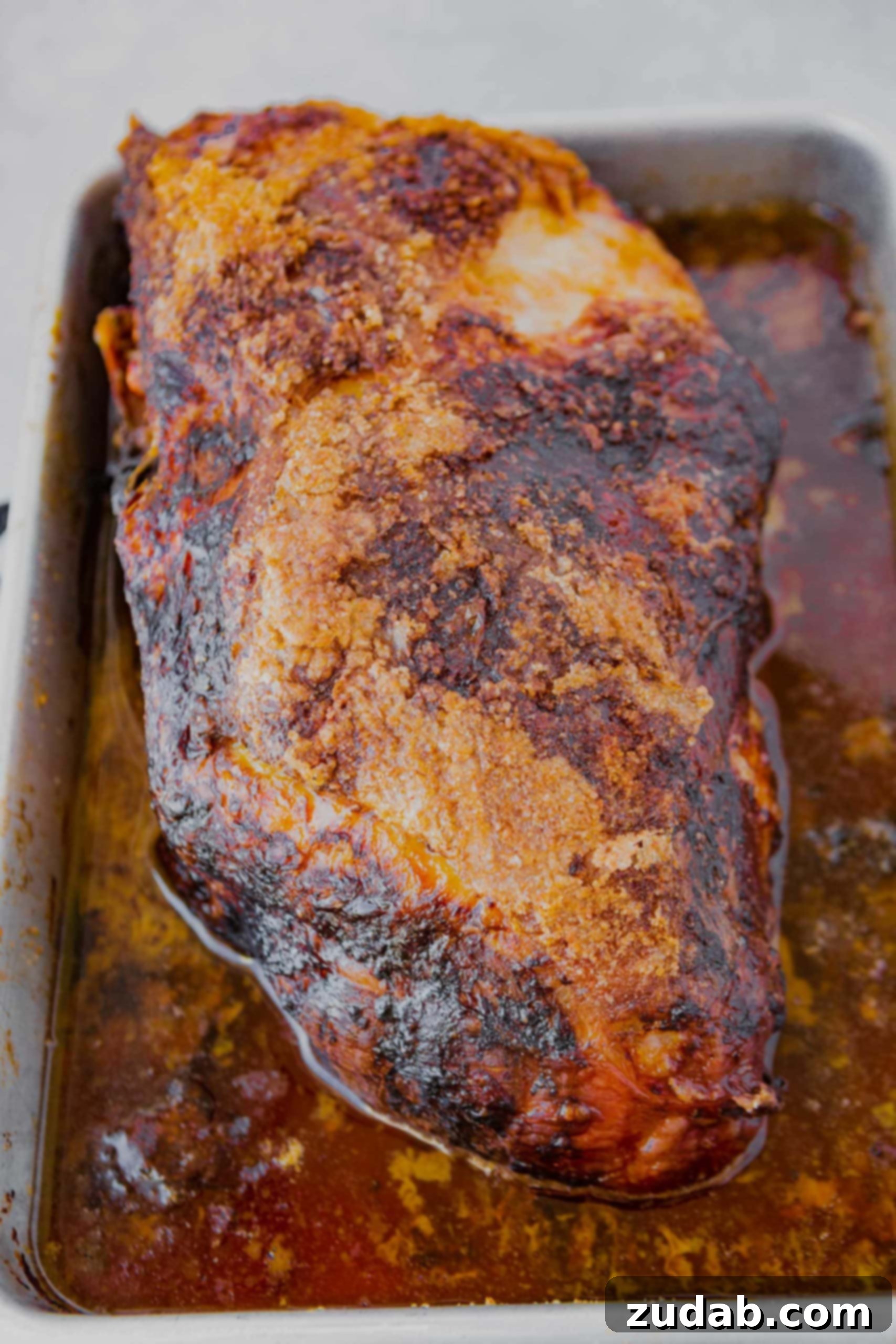 Slow Cooker Kalua Pork Recipe a perfectly roasted whole pork butt in a white baking dish sitting into its juices ready to be shredded
