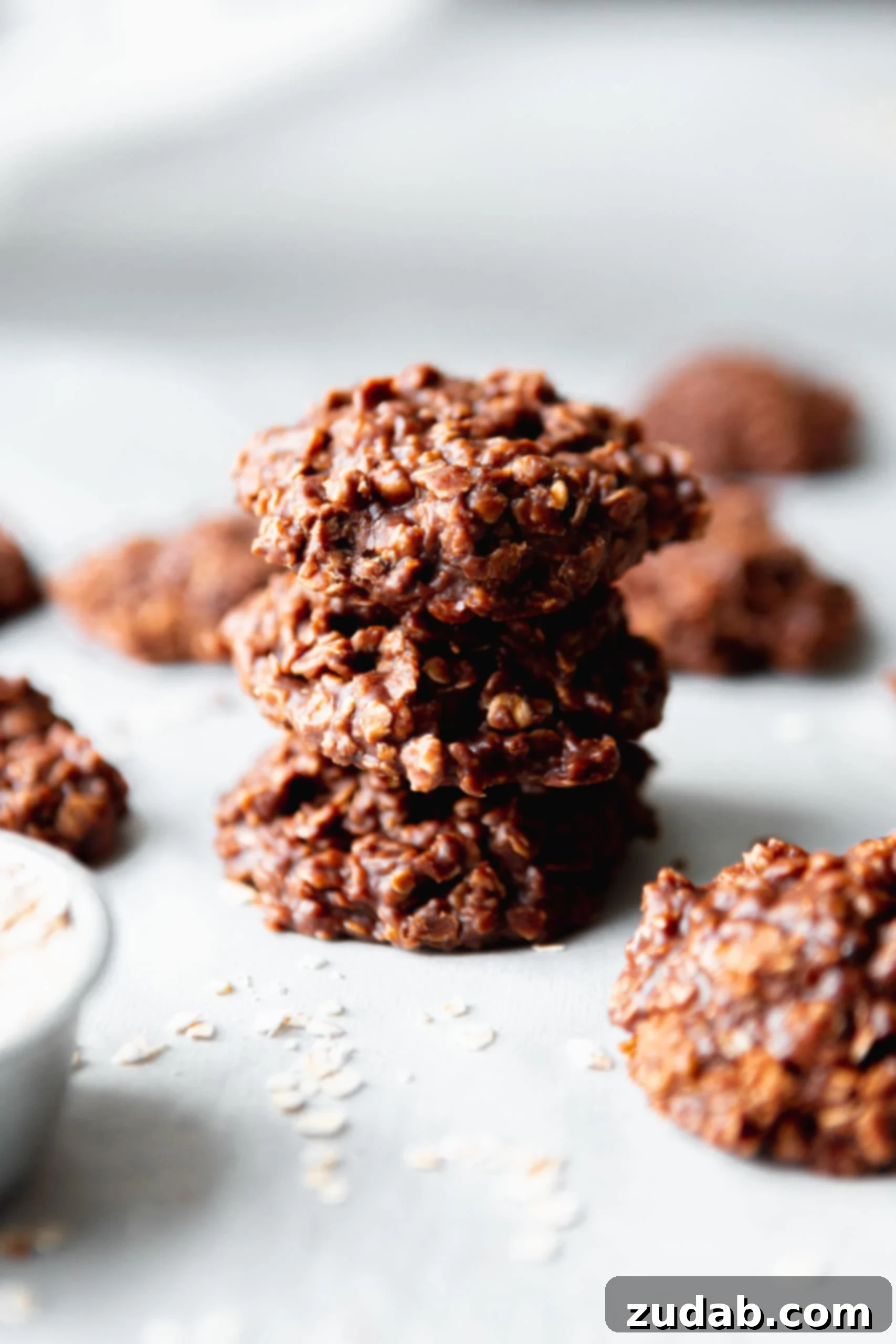 Three no bake cookies stacked on top of each other. They are chocolate and oatmeal. Other cookies are behind the stack.