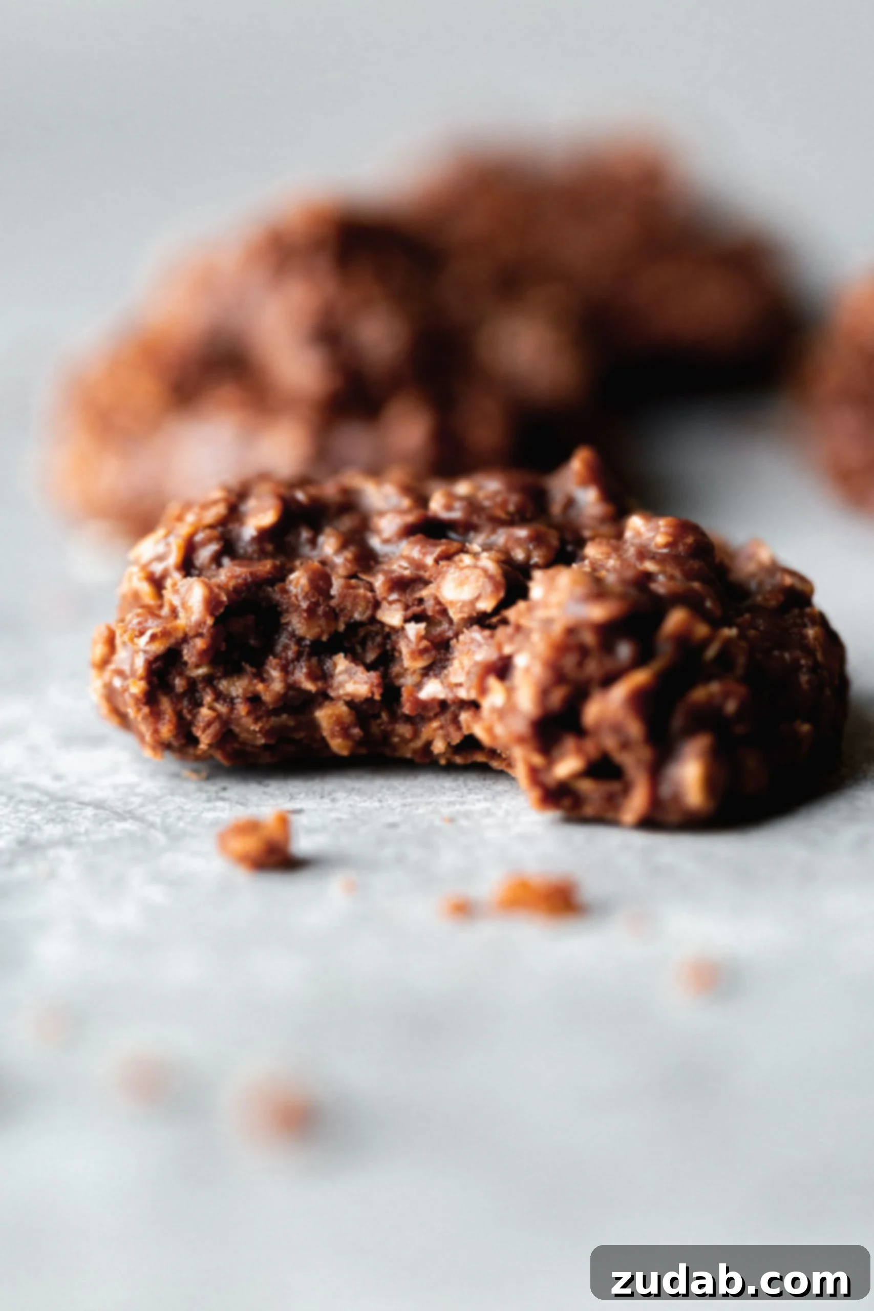 A chocolate no bake cookie with a bite taken out of it. The cookie is chocolate with oatmeal.