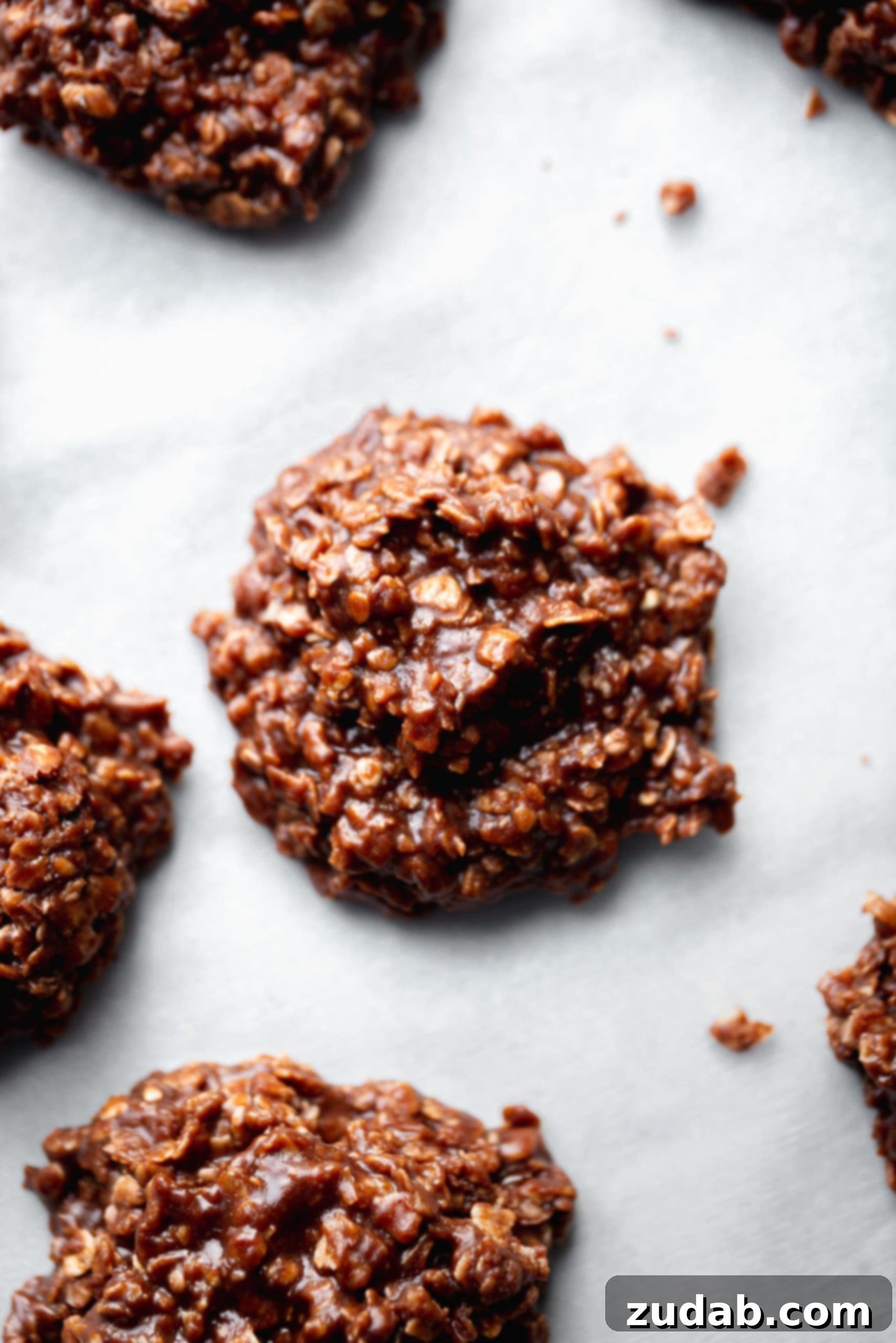 Chocolate no bake cookies on parchment paper. You can see the oats mixed into the chocolaty goodness.