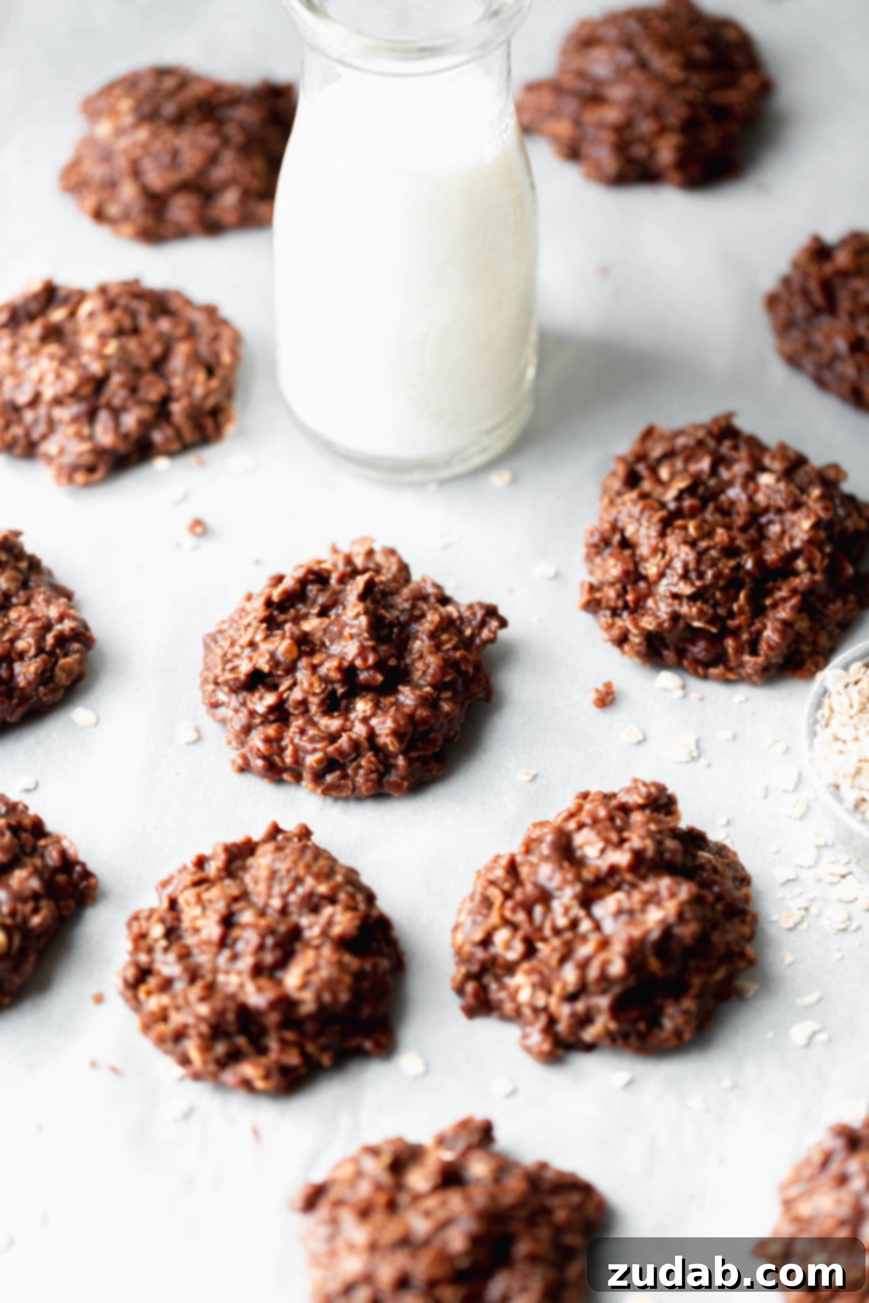  Chocolate peanut butter no bake cookies on parchment paper. You can see the oats mixed in chocolate. There is a glass of milk next to the cookies.