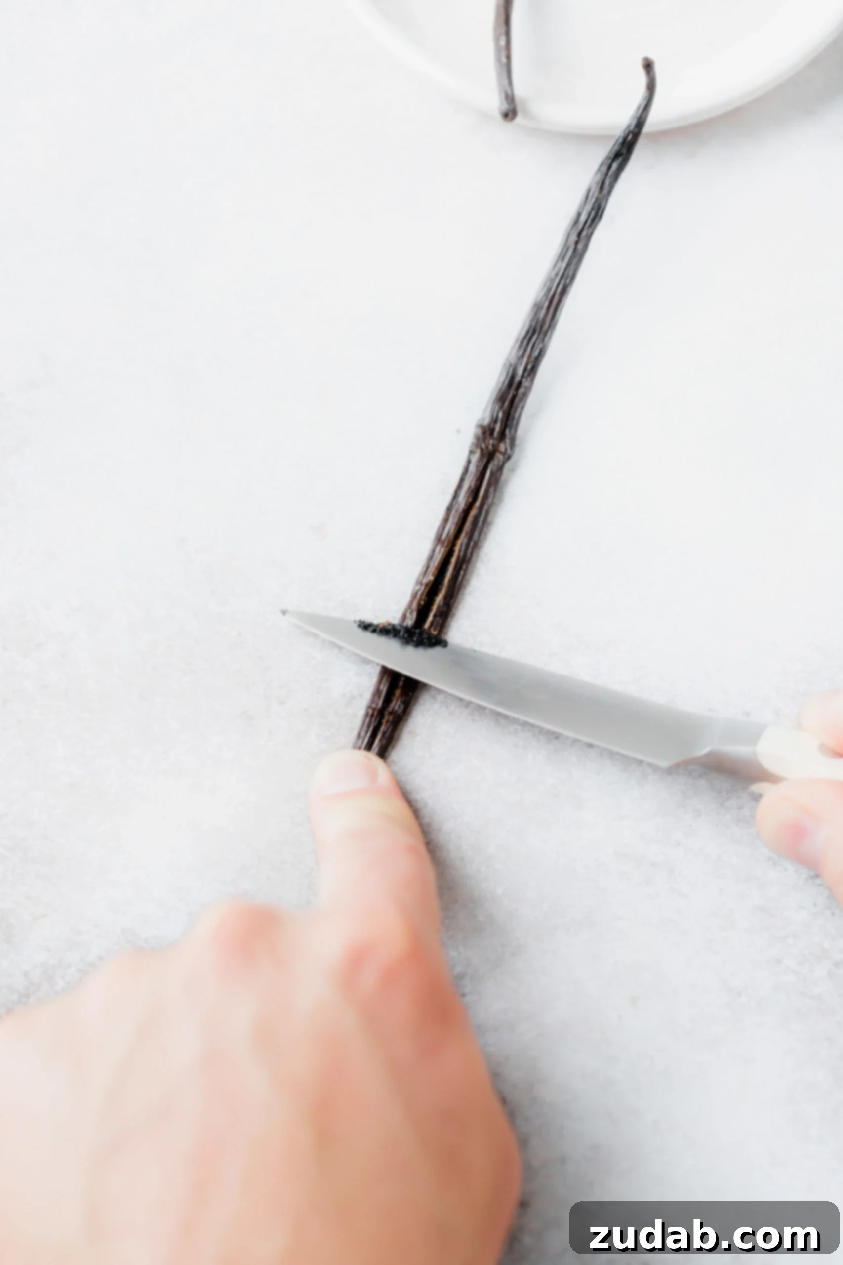 Vanilla Bean Whipped Cream A vanilla bean pod with the beans being scraped out with a knife.