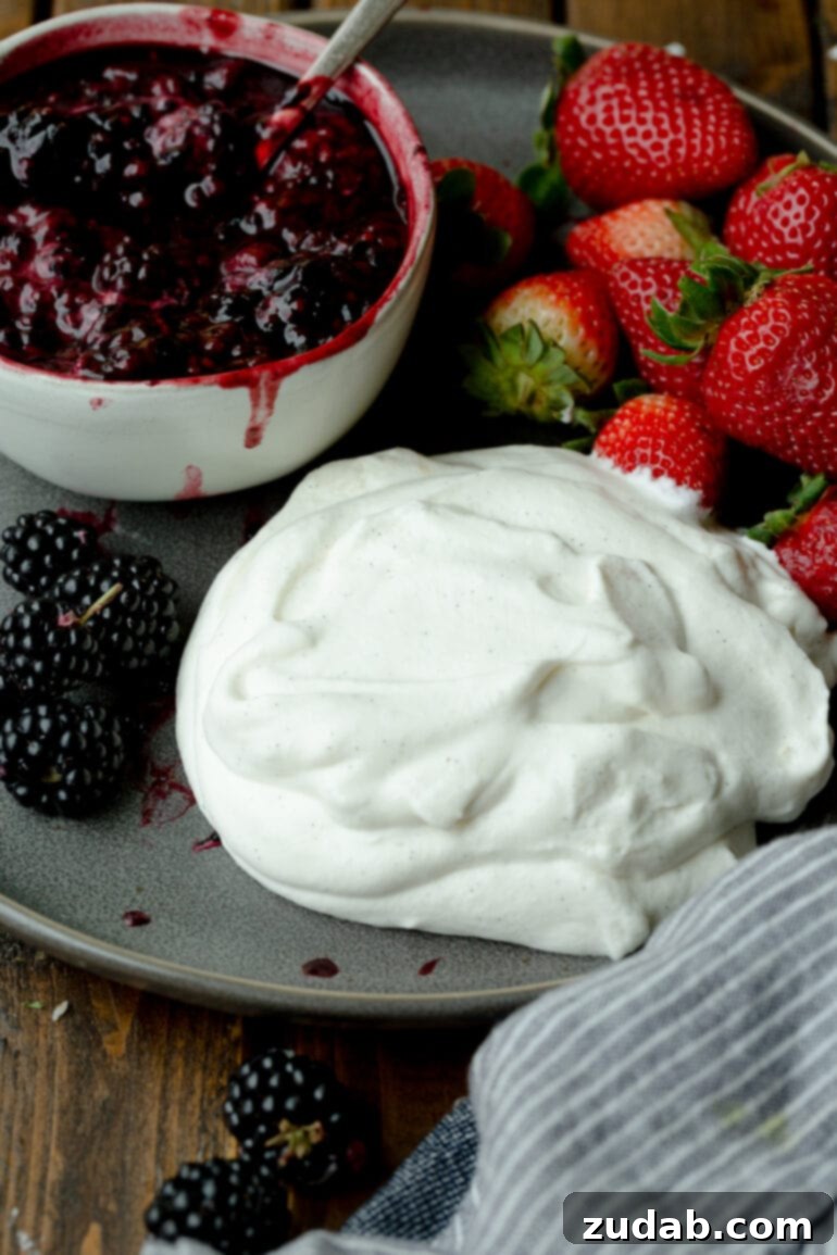 Dreamy Vanilla Bean Whipped Cream 3 a photo of a vanilla bean whipped cream on a plate next to several fresh berries and a bowl of berry sauce.