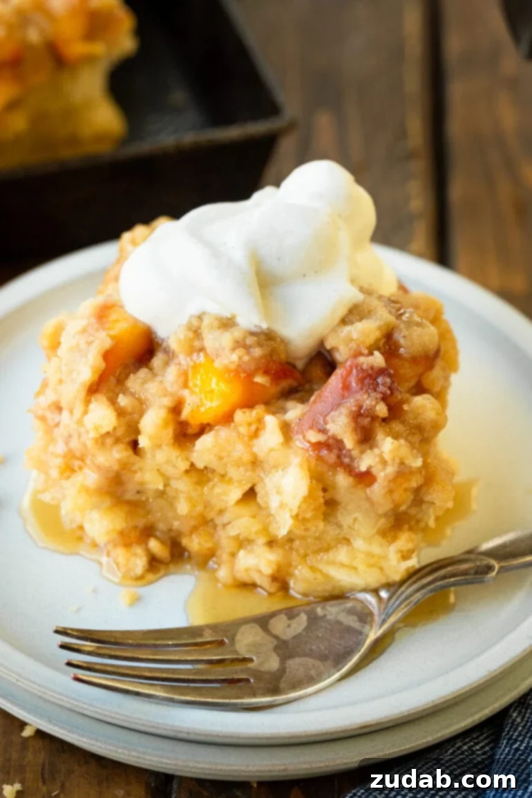 Delicious Peach Cobbler French Toast 2 A photo of a serving of golden baked peach cobbler french toast casserole topped with a dollop of whipped cream, showcasing its irresistible crumb topping and juicy peach filling.