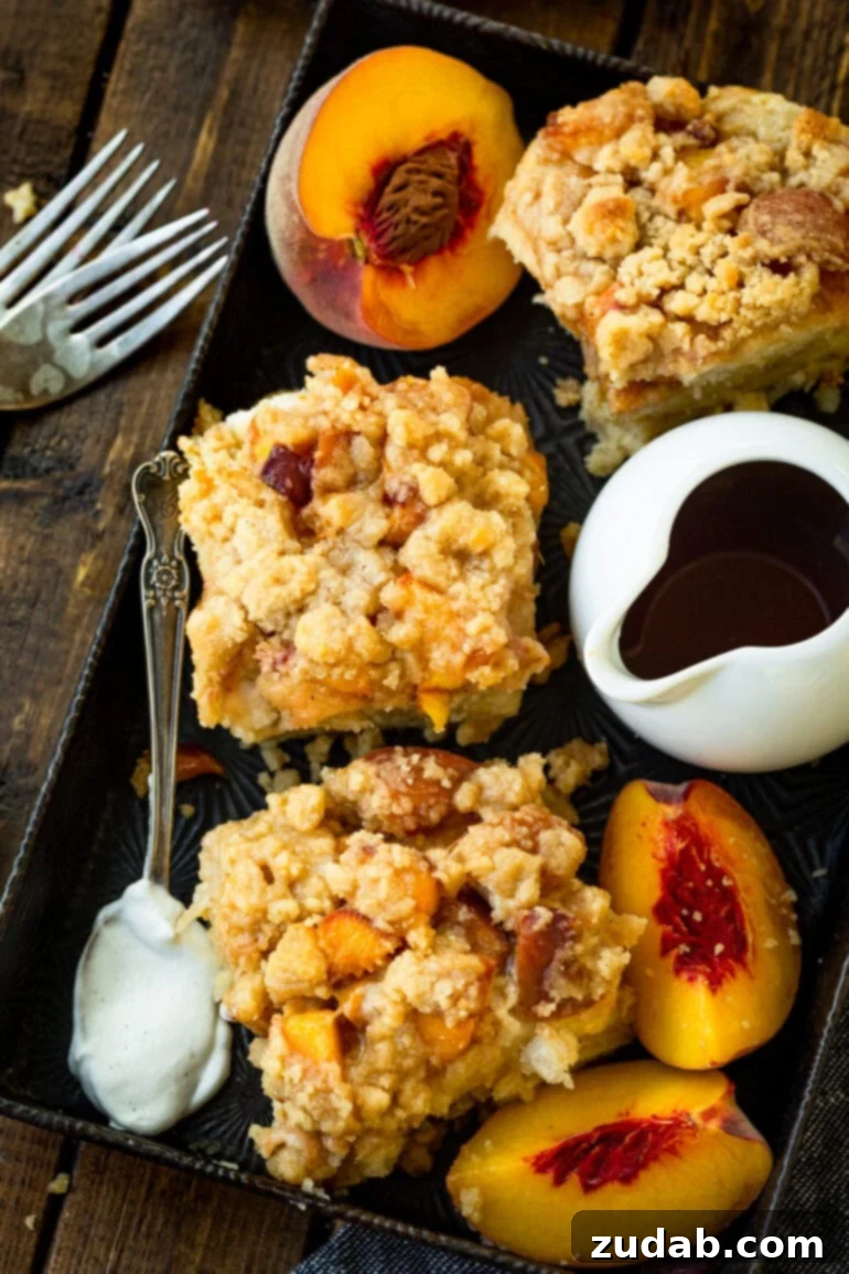 Delicious Peach Cobbler French Toast 3 A photo of several servings of peach french toast casserole topped with a streusel topping, accompanied by a container of syrup and slices of fresh peaches, emphasizing its visual appeal.